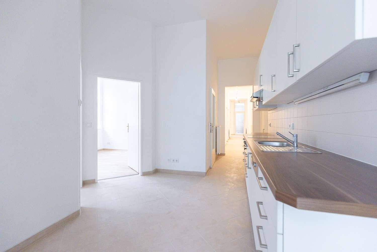 Funktionale Küche mit weißen Schränken, Holz-Arbeitsplatte und Fliesenboden, gut gepflegt.