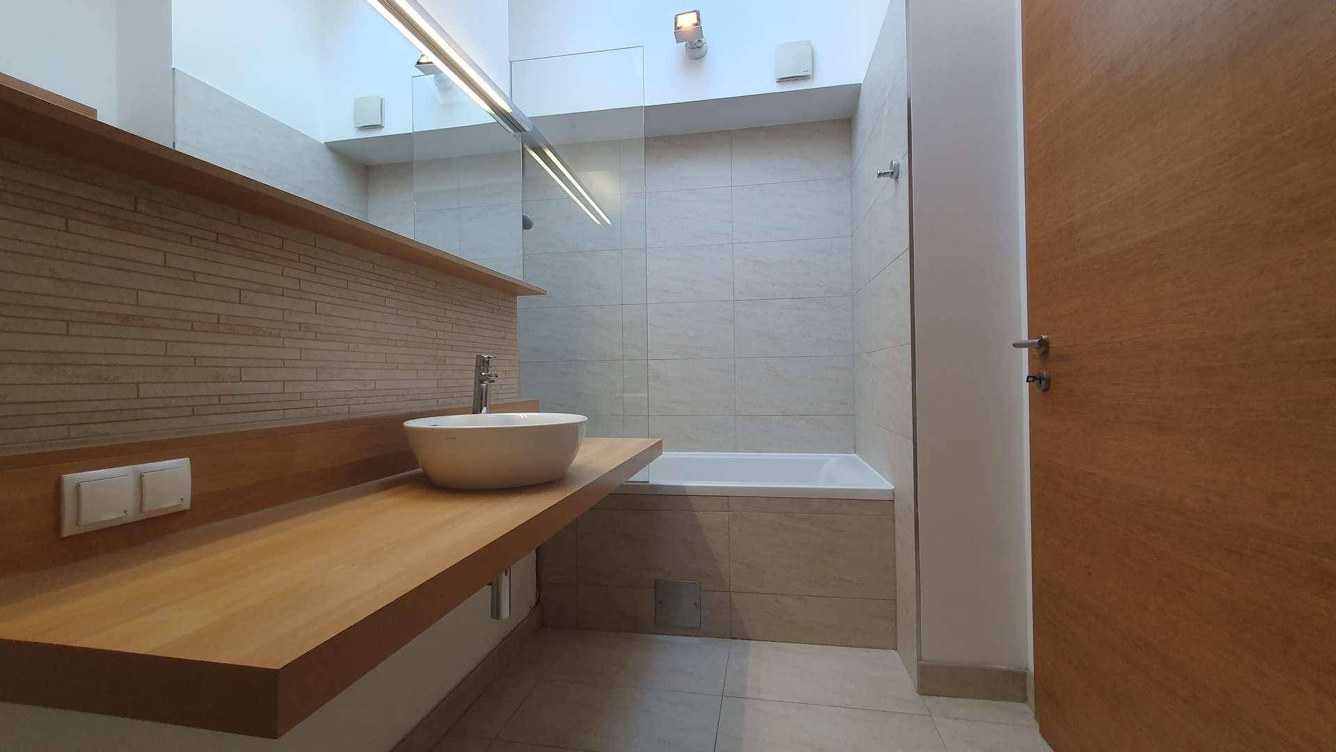 Modernes Badezimmer mit Badewanne, Aufsatzwaschbecken und Holzwaschtisch, hell gefliest und gut beleuchtet.