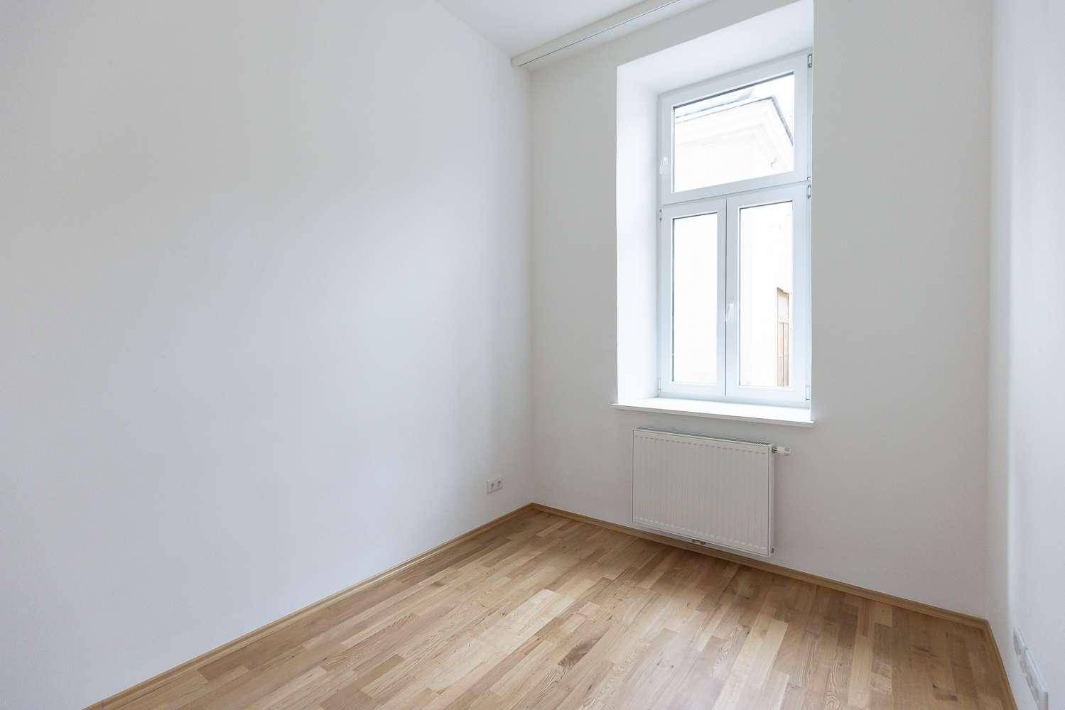 Helles, leeres Zimmer mit Parkettboden und einem Fenster, ideal als Schlaf- oder Arbeitszimmer.
