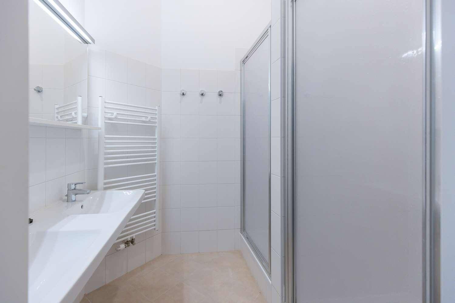 Modernes Badezimmer mit Waschbecken, Spiegelschrank, Duschkabine und Handtuchheizkörper.