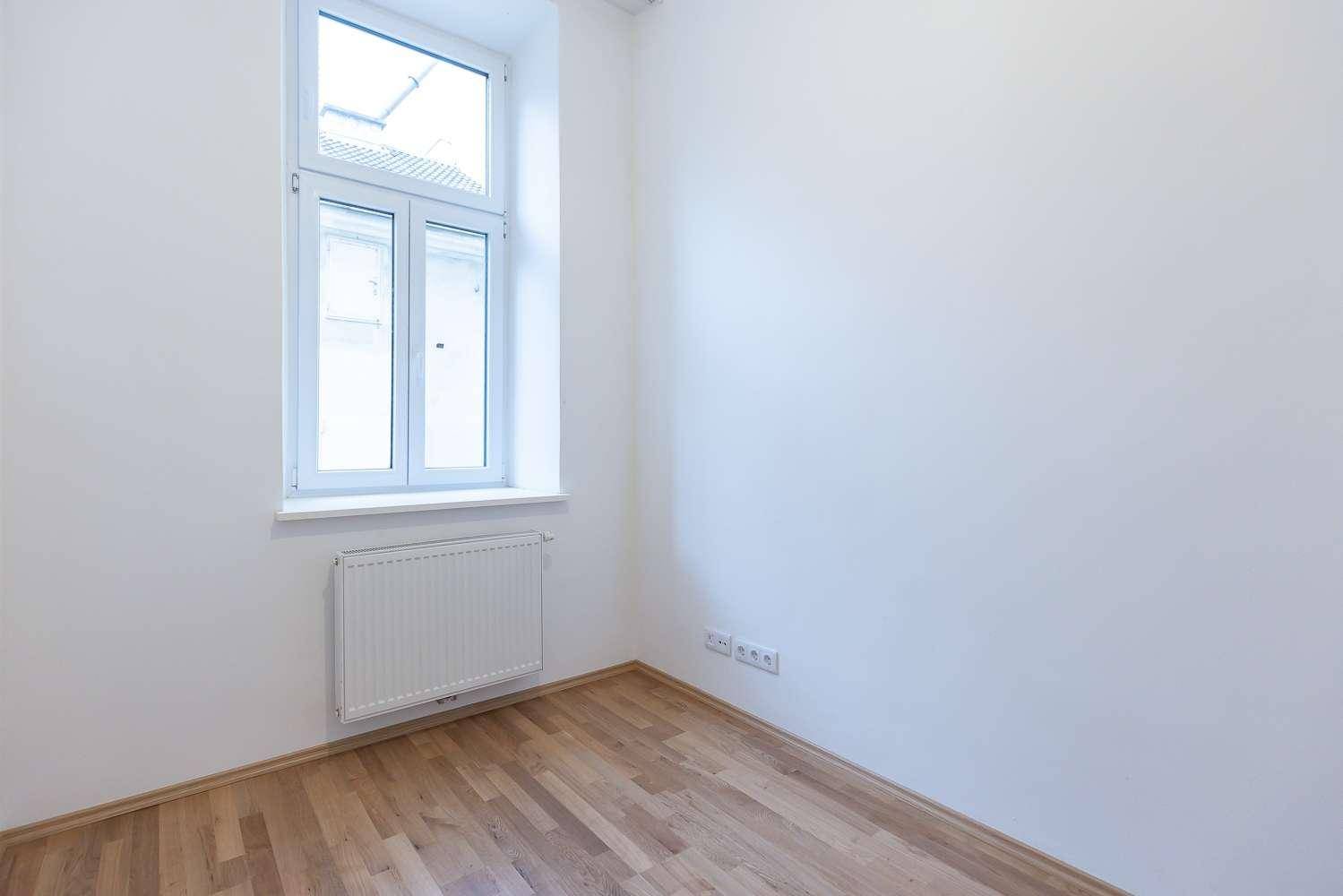 Helles Zimmer mit Parkettboden, weißen Wänden und einem Fenster, das für eine angenehme Atmosphäre sorgt.