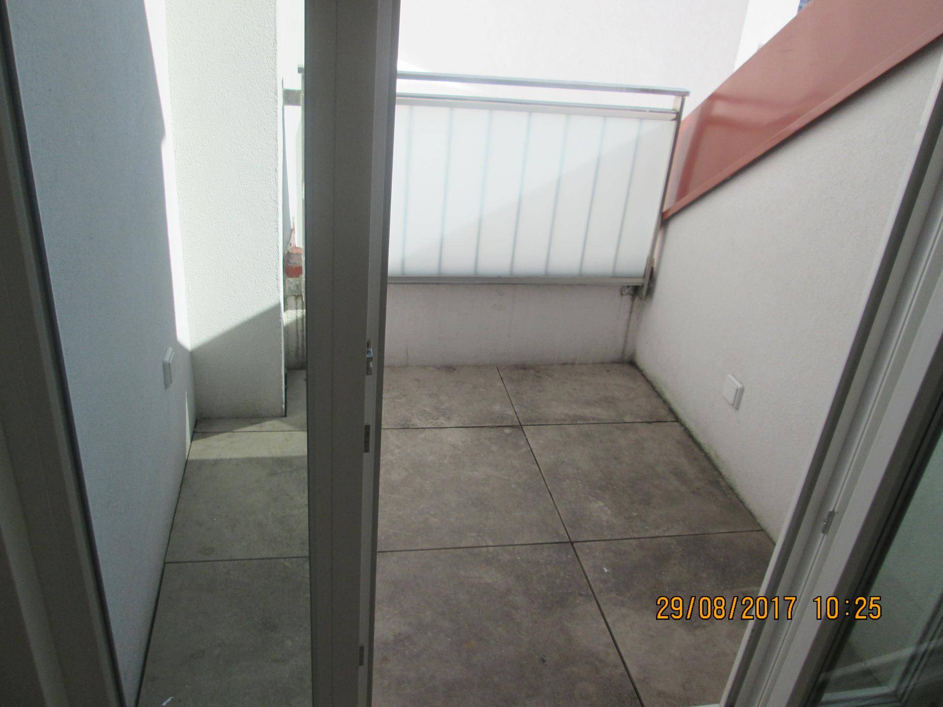 Kleine, geflieste Terrasse mit Sichtschutz und Zugang durch eine Glastür.