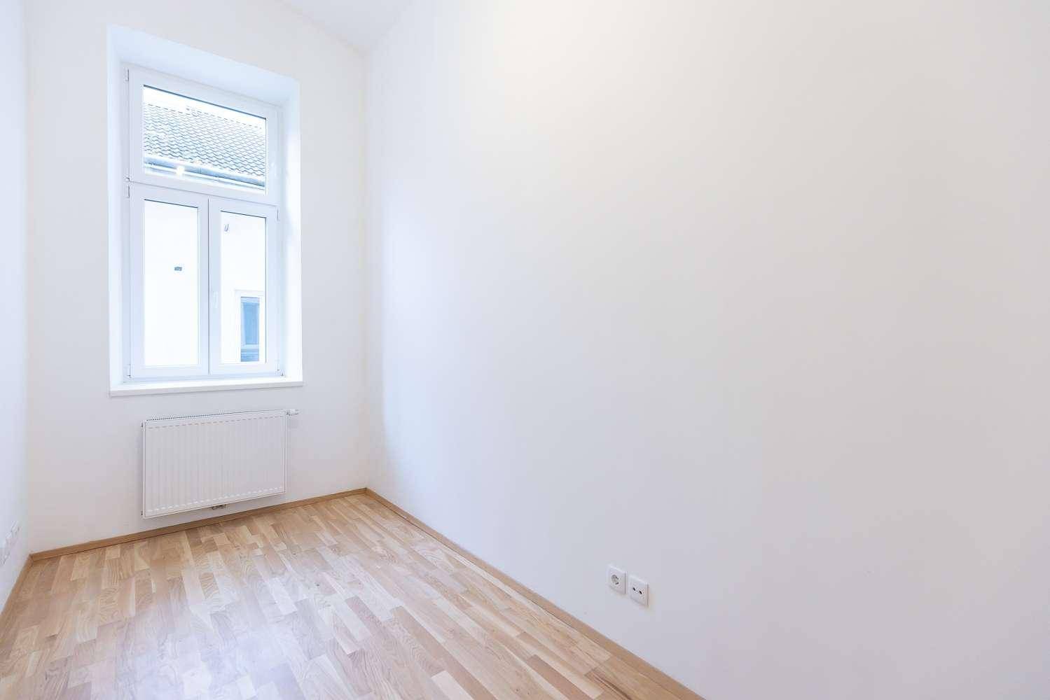 Geräumiges Zimmer mit hellem Parkettboden, weißen Wänden und einem großen Fenster.