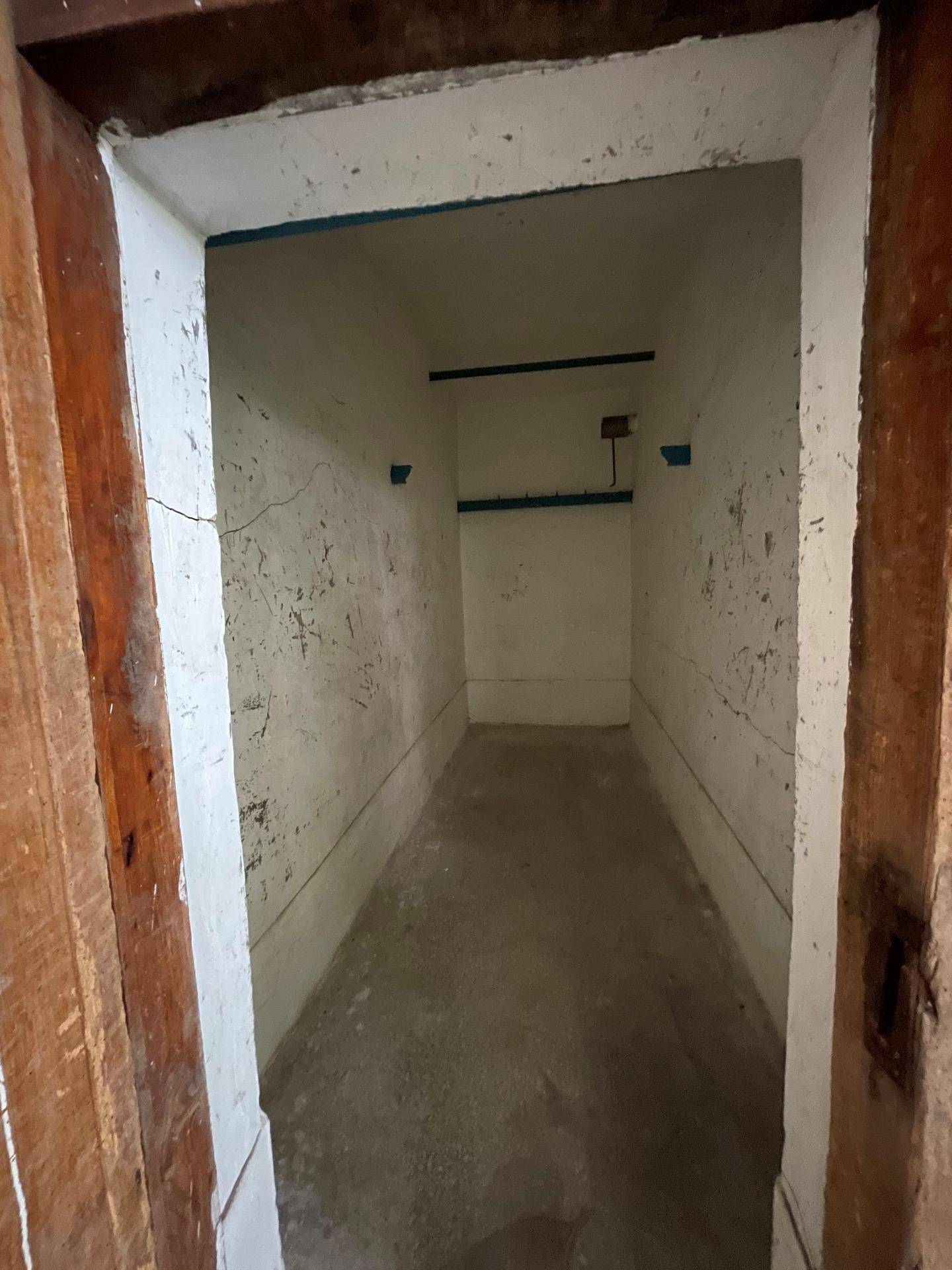 Kleiner, leerer Abstellraum im Keller mit einfachen, weißen Wänden und einem rohen Betonboden.