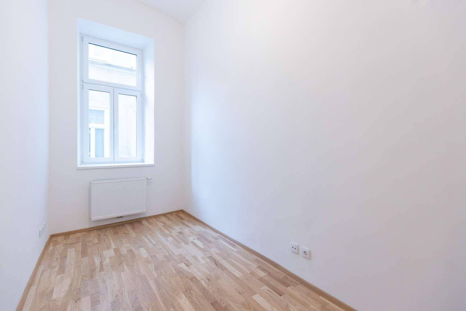 Gemütliches Schlafzimmer mit hellem Parkettboden, weißen Wänden und einem Fenster.