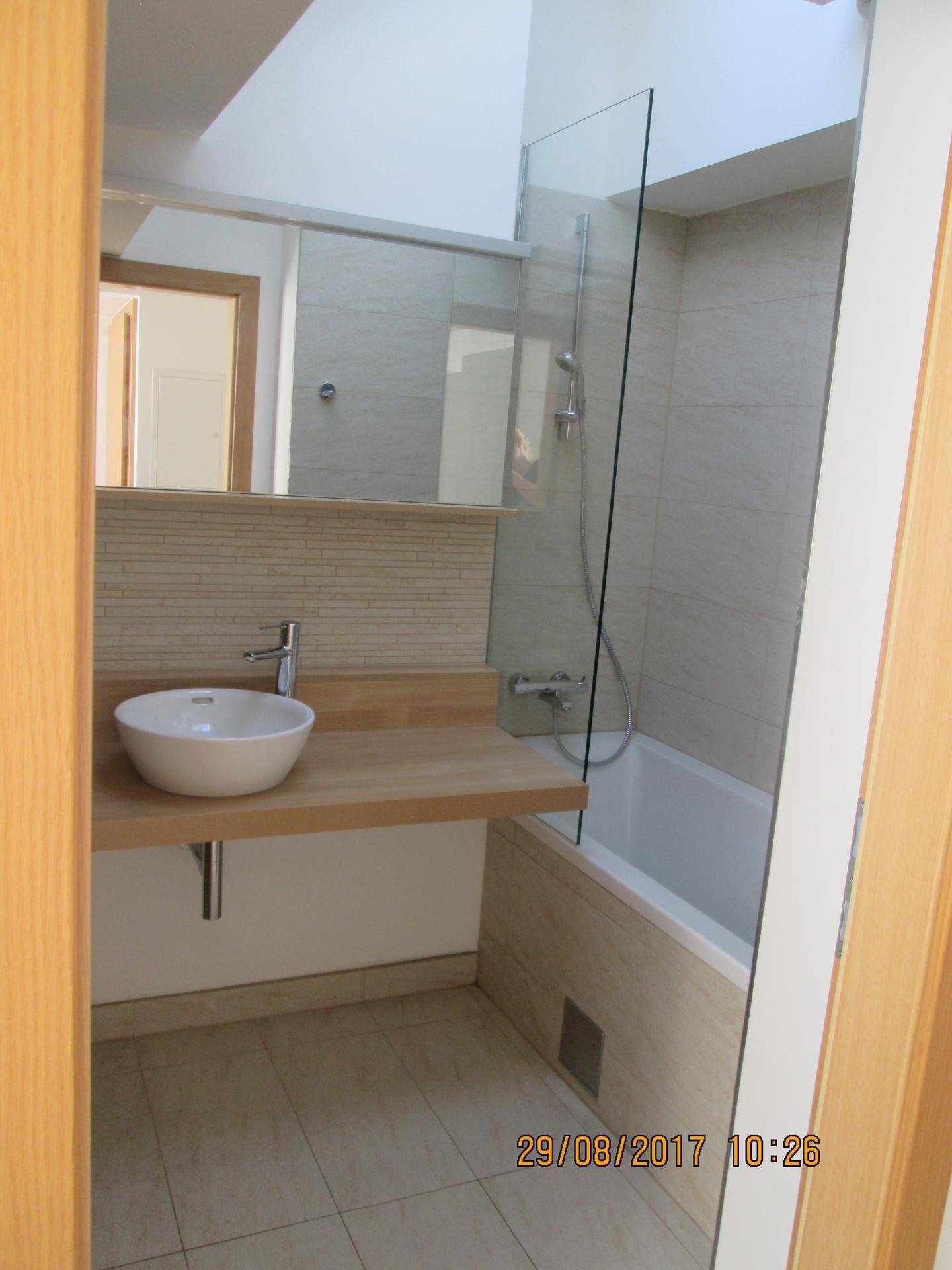Helles Badezimmer mit Badewanne, Waschbecken auf Holzplatte und Dachfenster für natürliches Licht.