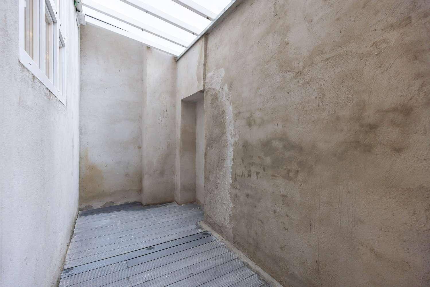 Kleiner überdachter Außenbereich mit Holzboden und rauen Wänden, ideal zum Entspannen.