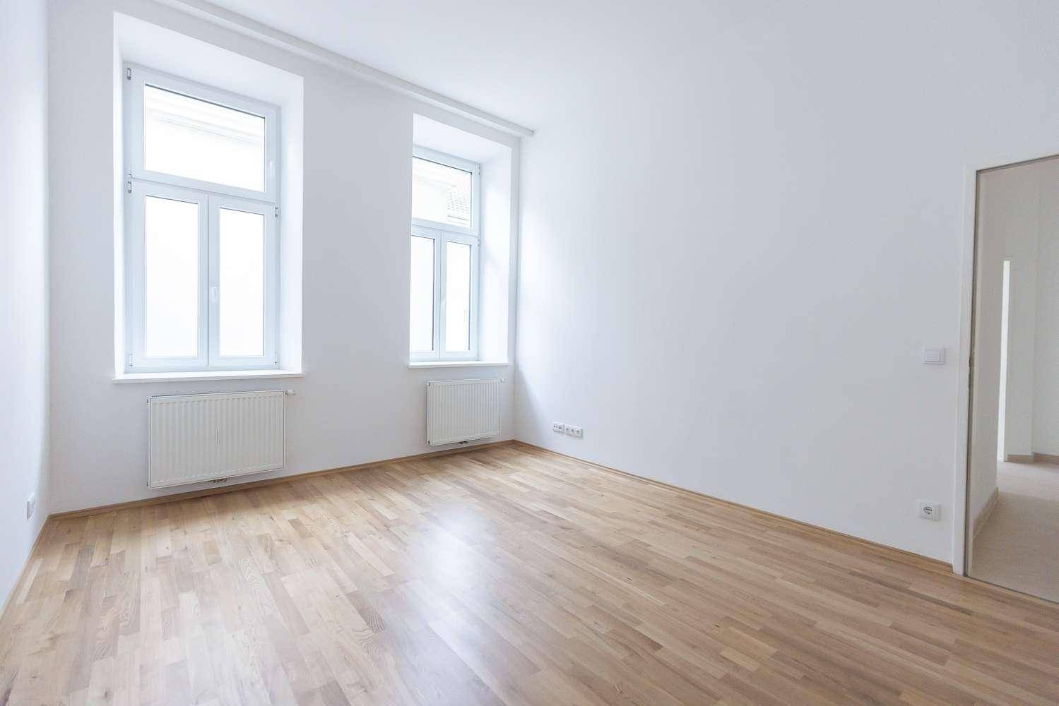 Heller und geräumiger Wohnbereich mit Parkettboden und zwei großen Fenstern, offen gestaltet.