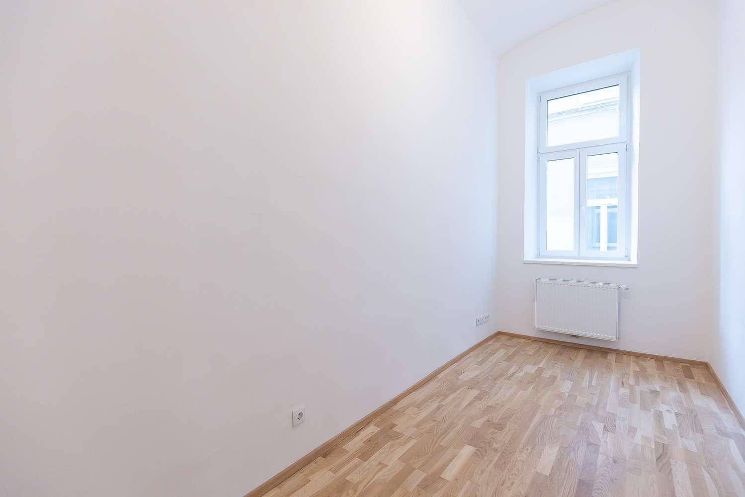 Helles Schlafzimmer mit Parkettboden, weißen Wänden und einem großen Fenster für viel Tageslicht.
