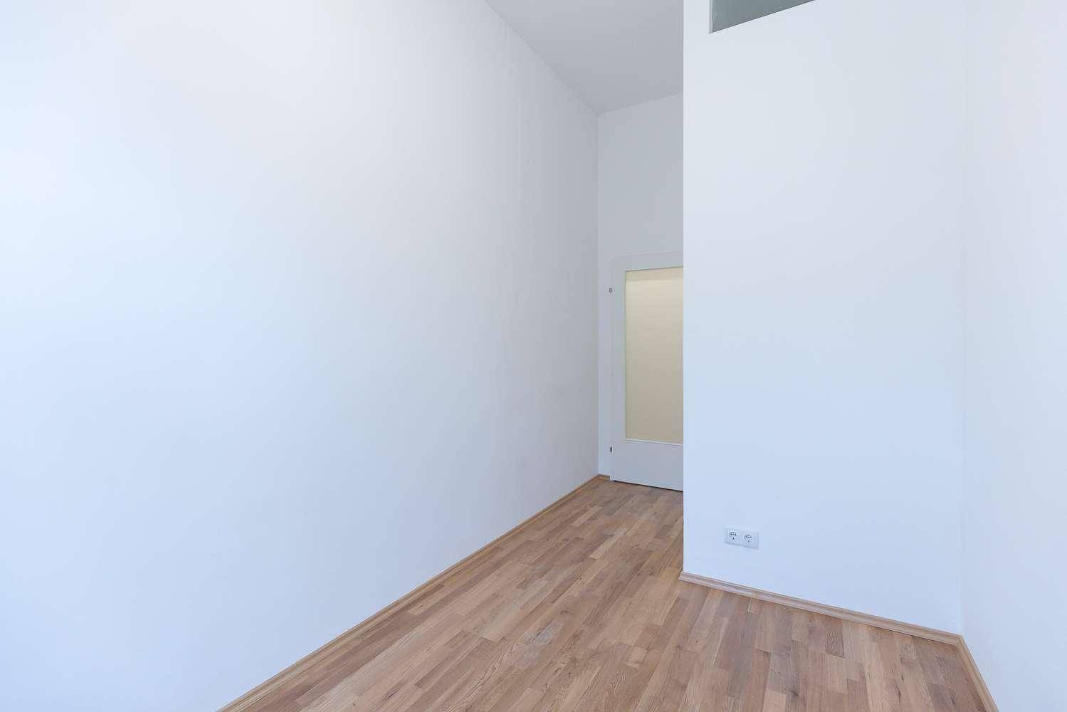 Helles Zimmer mit Parkettboden, weißen Wänden und einem Durchgang zu einem weiteren Raum.