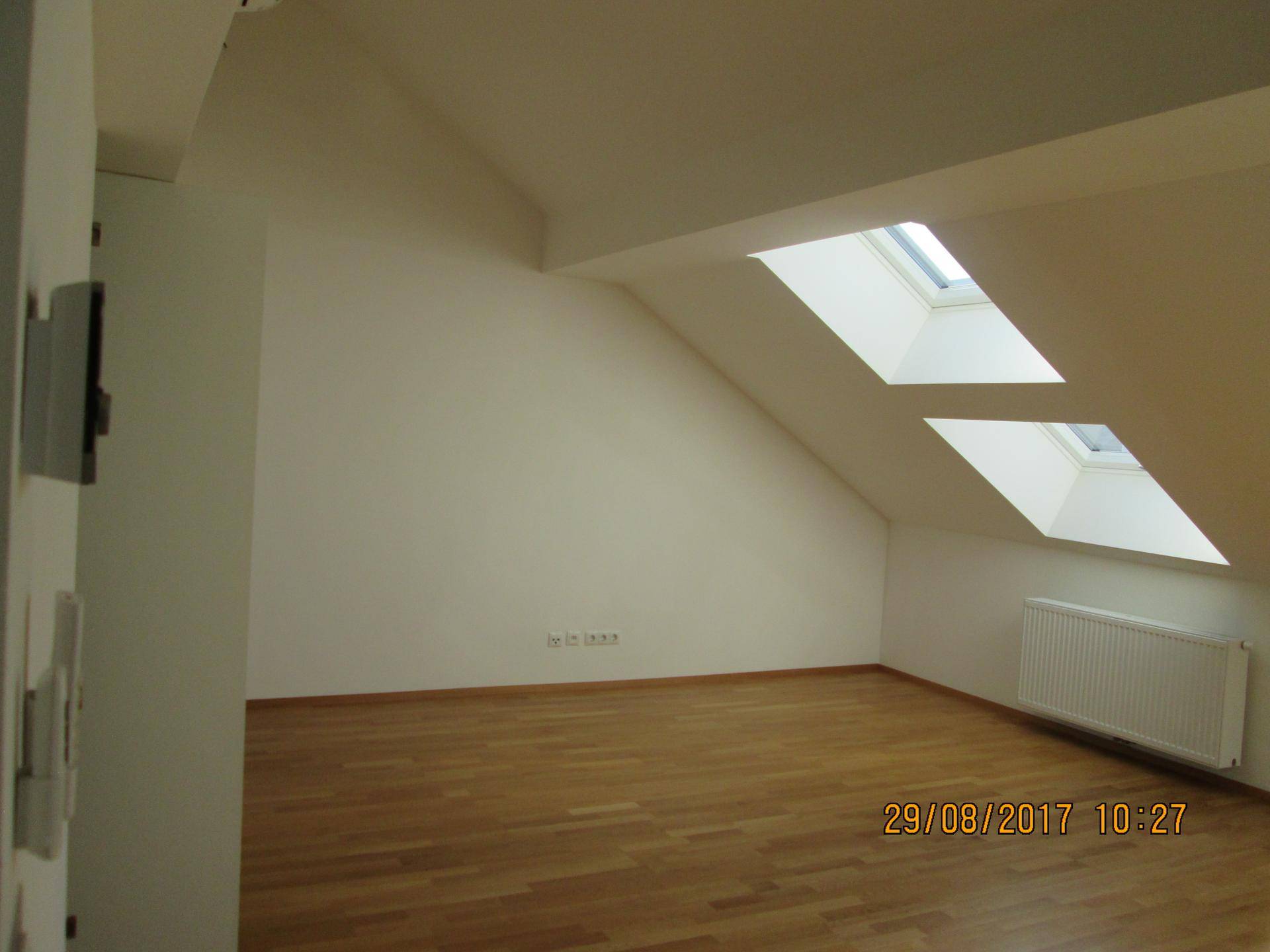 Schlafzimmer mit Holzparkett, Dachschräge und einem Heizkörper, bereit zur Einrichtung.