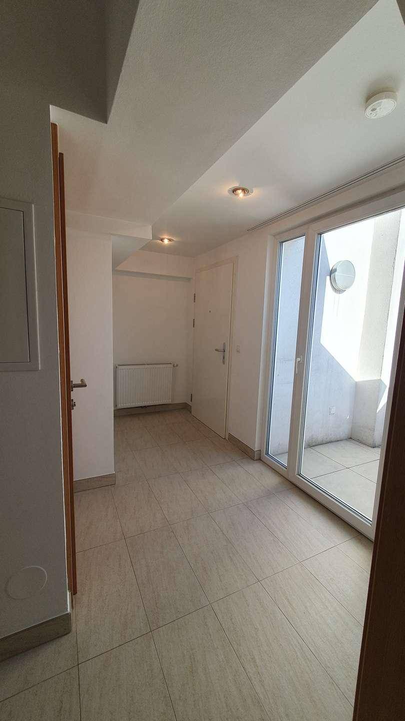 Heller Flur mit Fliesenboden und Zugang zu einem kleinen Balkon, der viel Tageslicht hereinlässt.