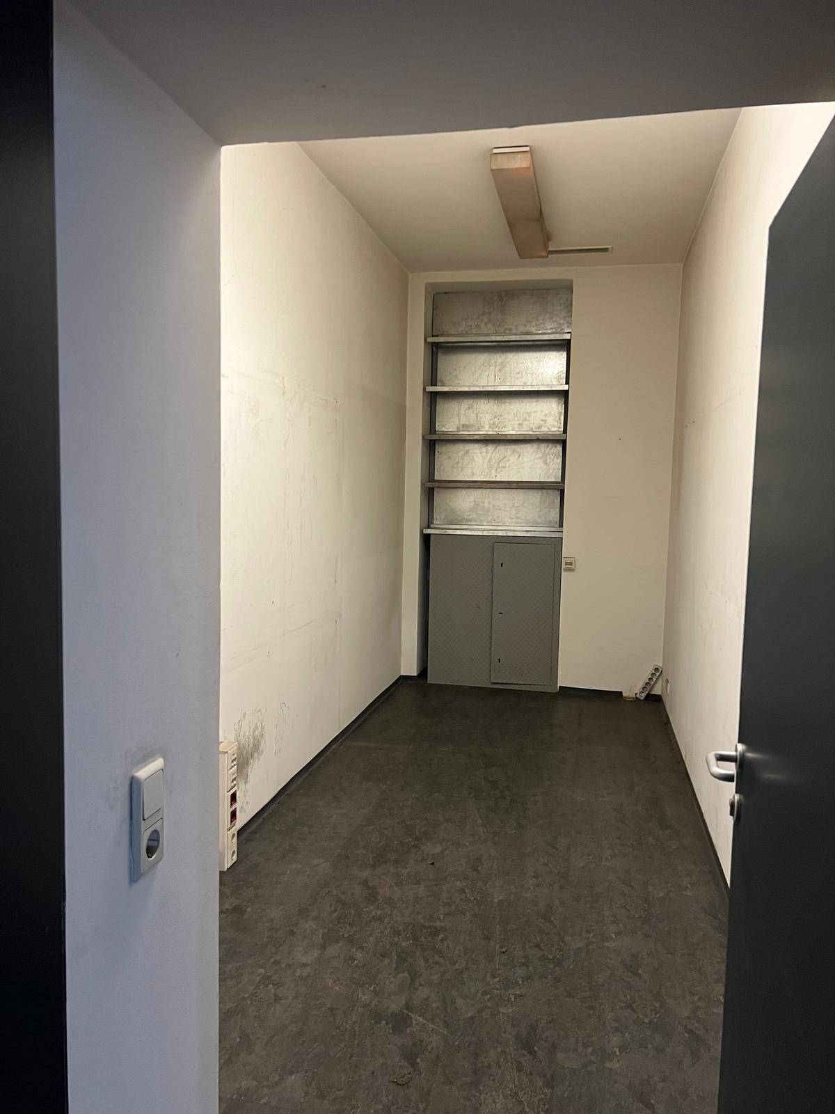 Kleiner, leerer Raum mit eingebauten Regalen und einem dunklen Boden, der als Abstellraum dienen könnte.