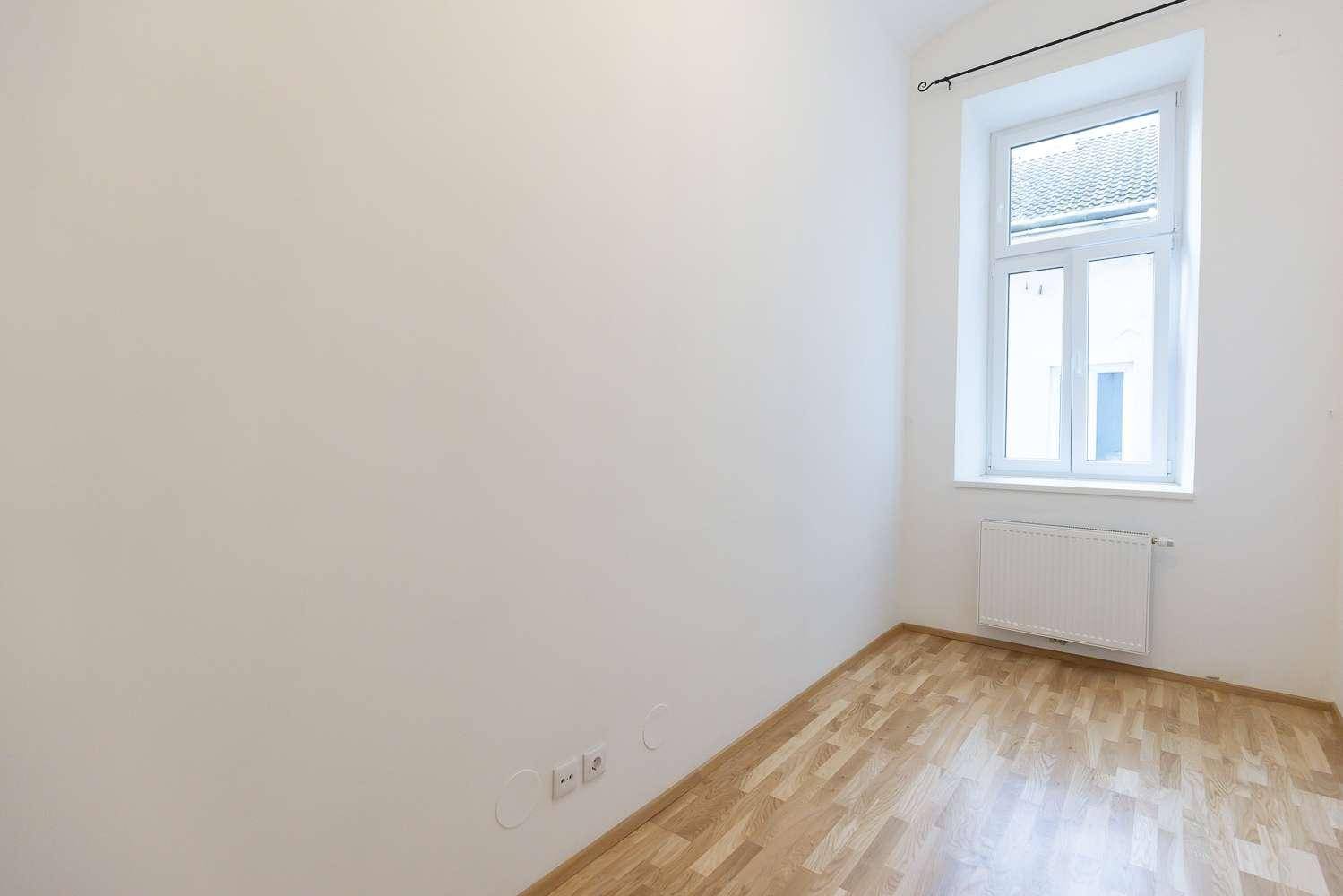 Helles Zimmer mit Parkettboden, weißen Wänden und einem Fenster, das viel Tageslicht hereinlässt.