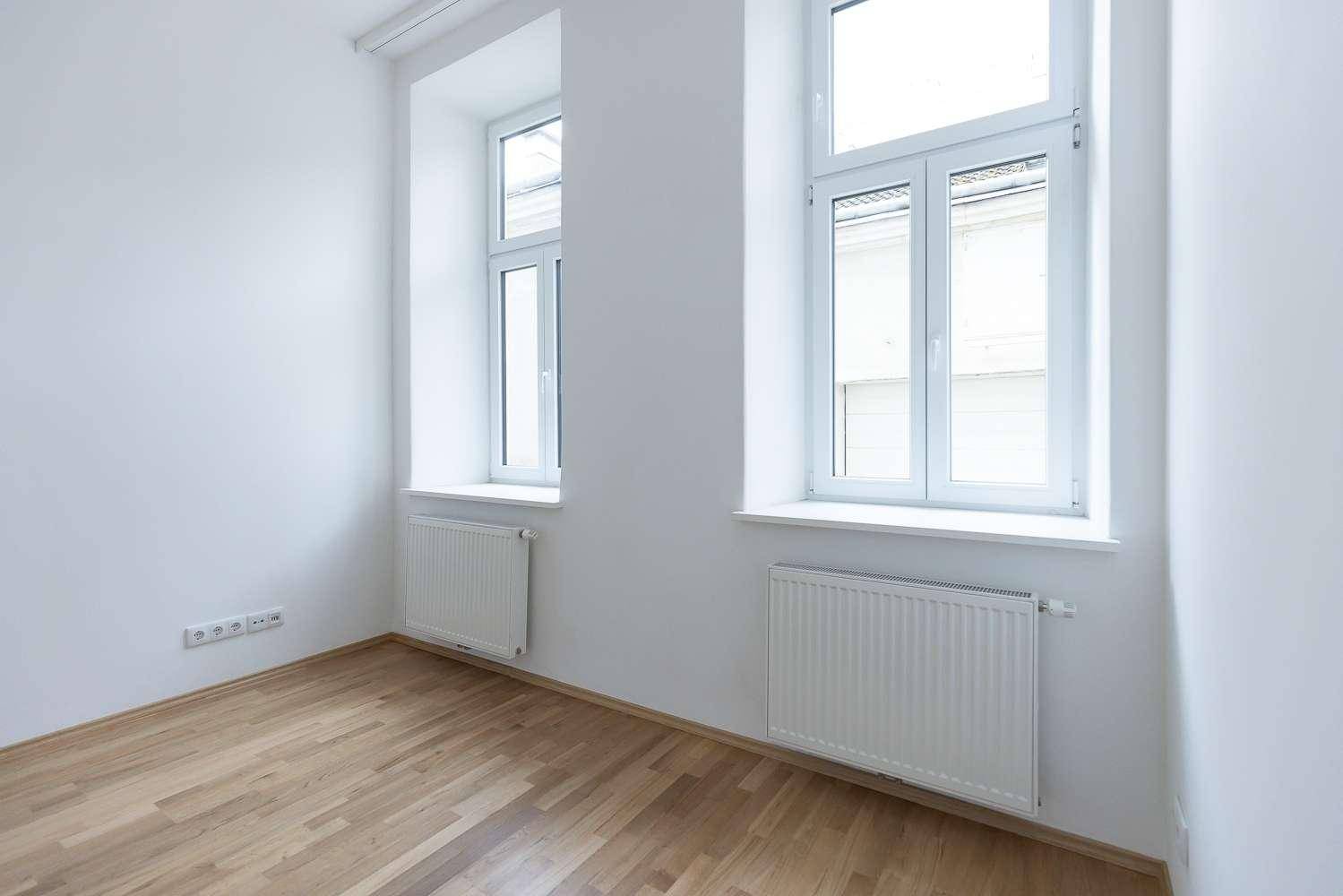 Geräumiges Zimmer mit hellem Parkettboden, weißen Wänden und zwei großen Fenstern.