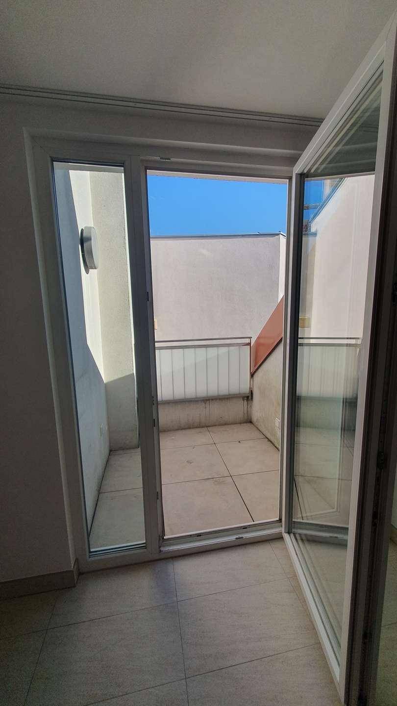 Kleiner, gefliester Balkon mit Glasbrüstung, zugänglich durch eine große Glastür, bietet einen privaten Außenbereich.