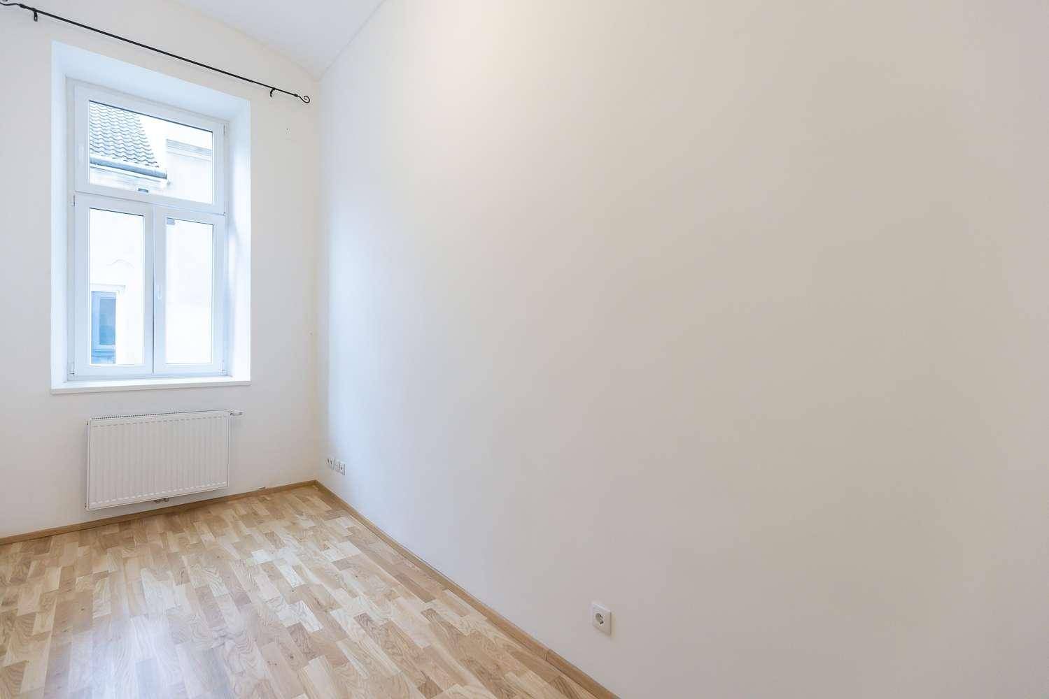 Helles Zimmer mit Parkettboden, weißen Wänden und einem Fenster mit Blick nach draußen.