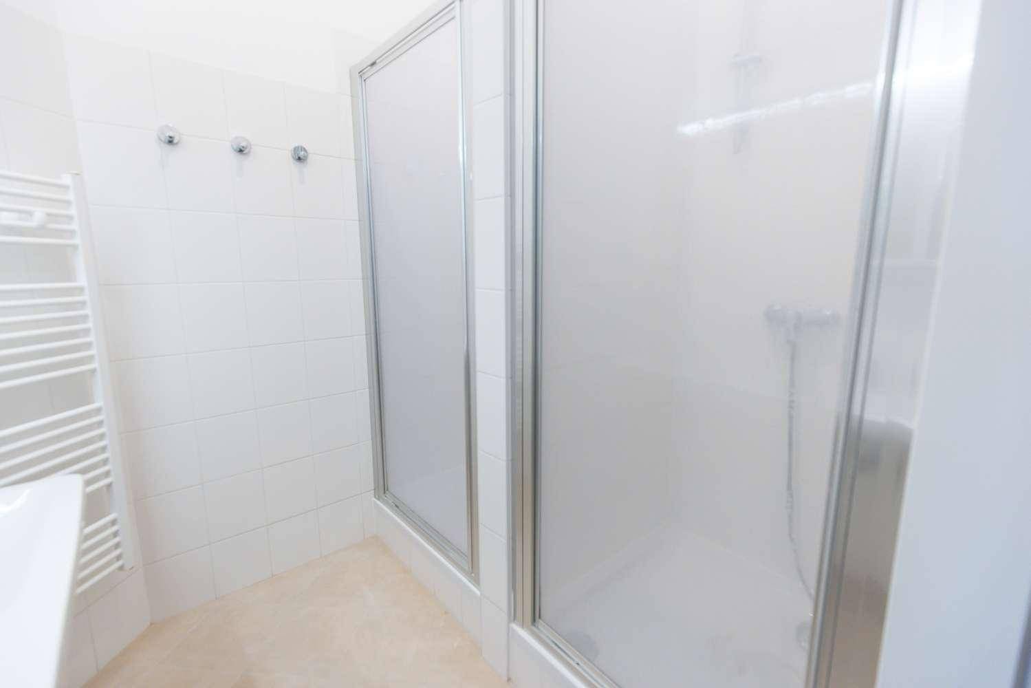 Helles Badezimmer mit Duschkabine, weißen Fliesen und einem praktischen Handtuchheizkörper.