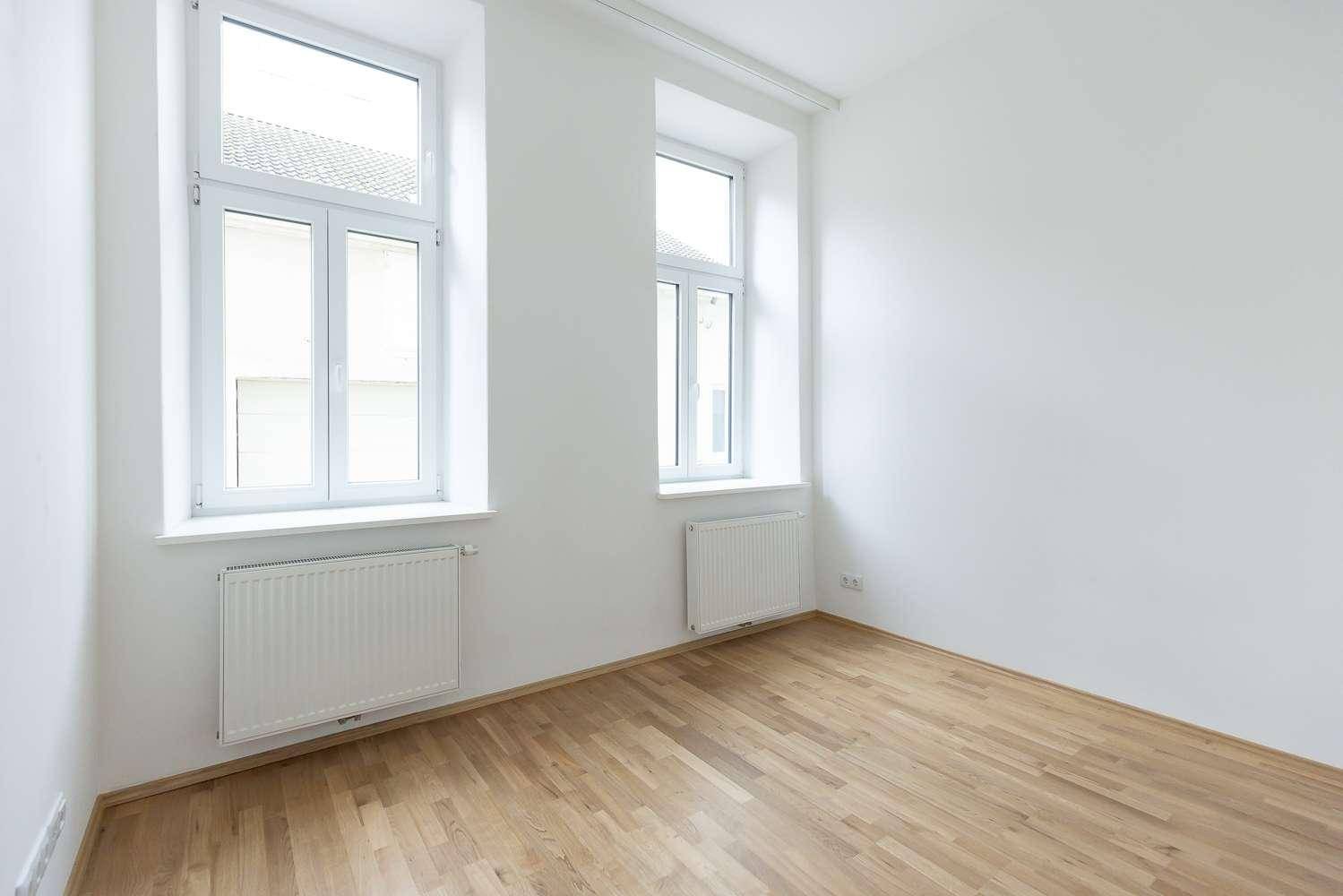 Helles Zimmer mit Parkettboden, weißen Wänden und zwei großen Fenstern für viel Tageslicht.
