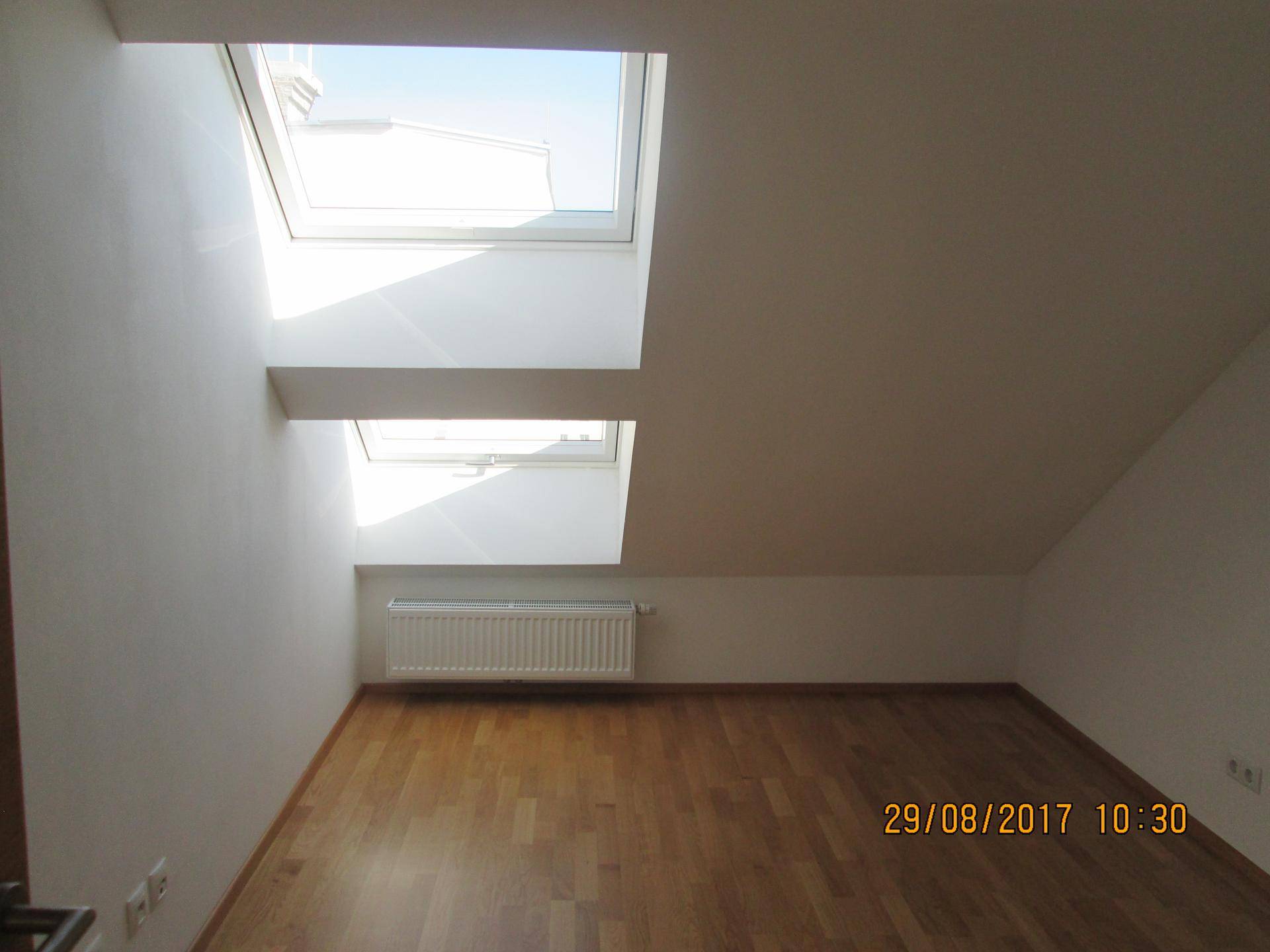 Helles Schlafzimmer mit Holzparkett, Dachschräge und zwei großen Dachfenstern.