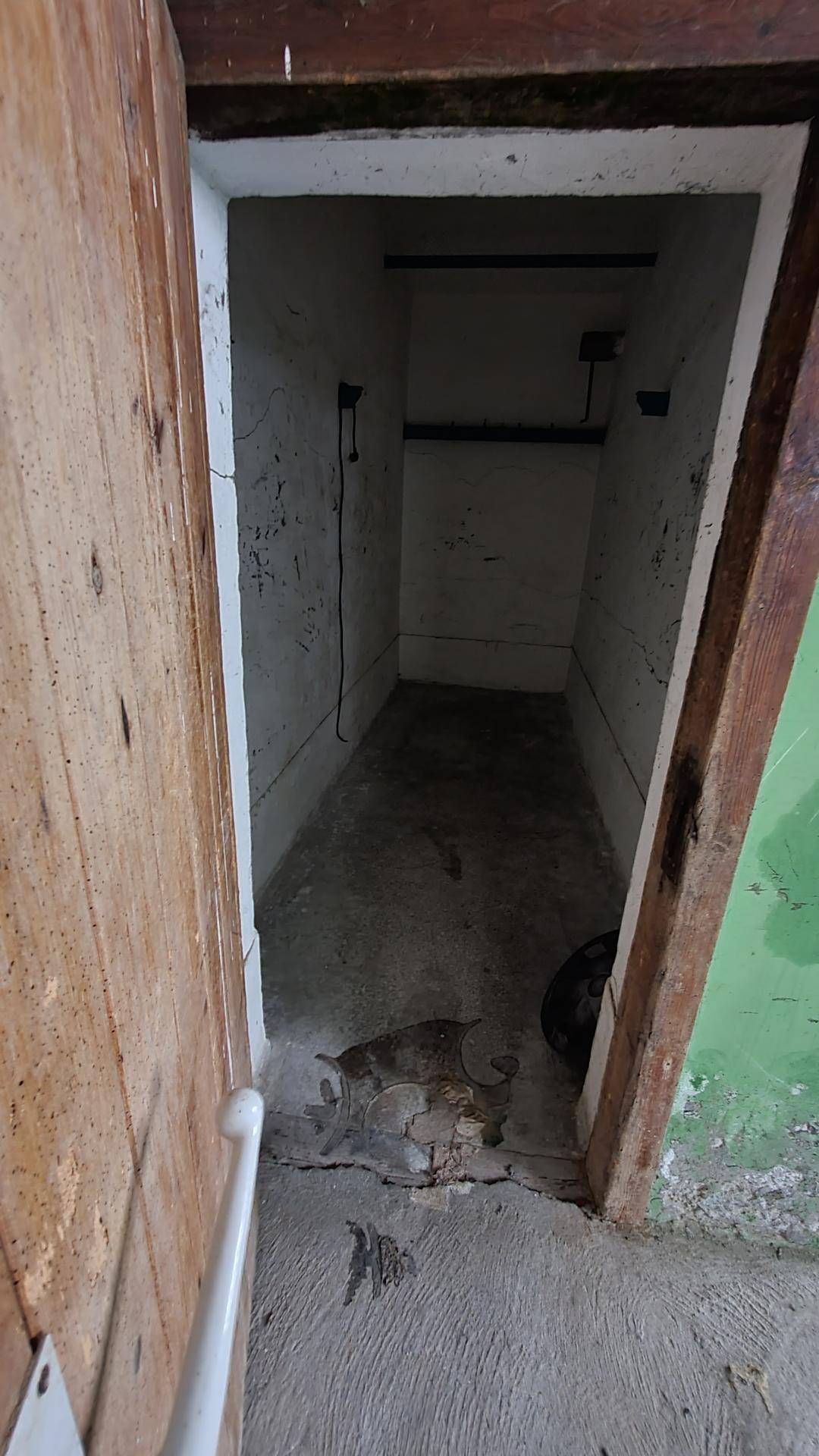 Kleiner, schmaler Abstellraum im Keller mit einfachen, weißen Wänden und einem rohen Betonboden.