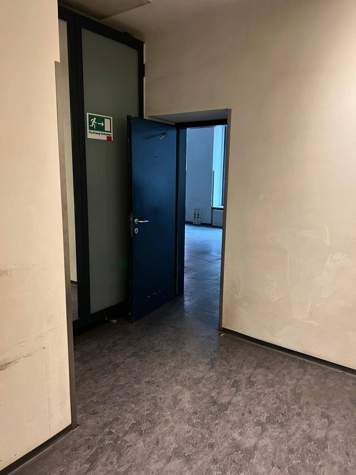 Flur mit dunklem Boden und einer offenen Tür, die zu einem helleren Bereich mit großen Fenstern führt.