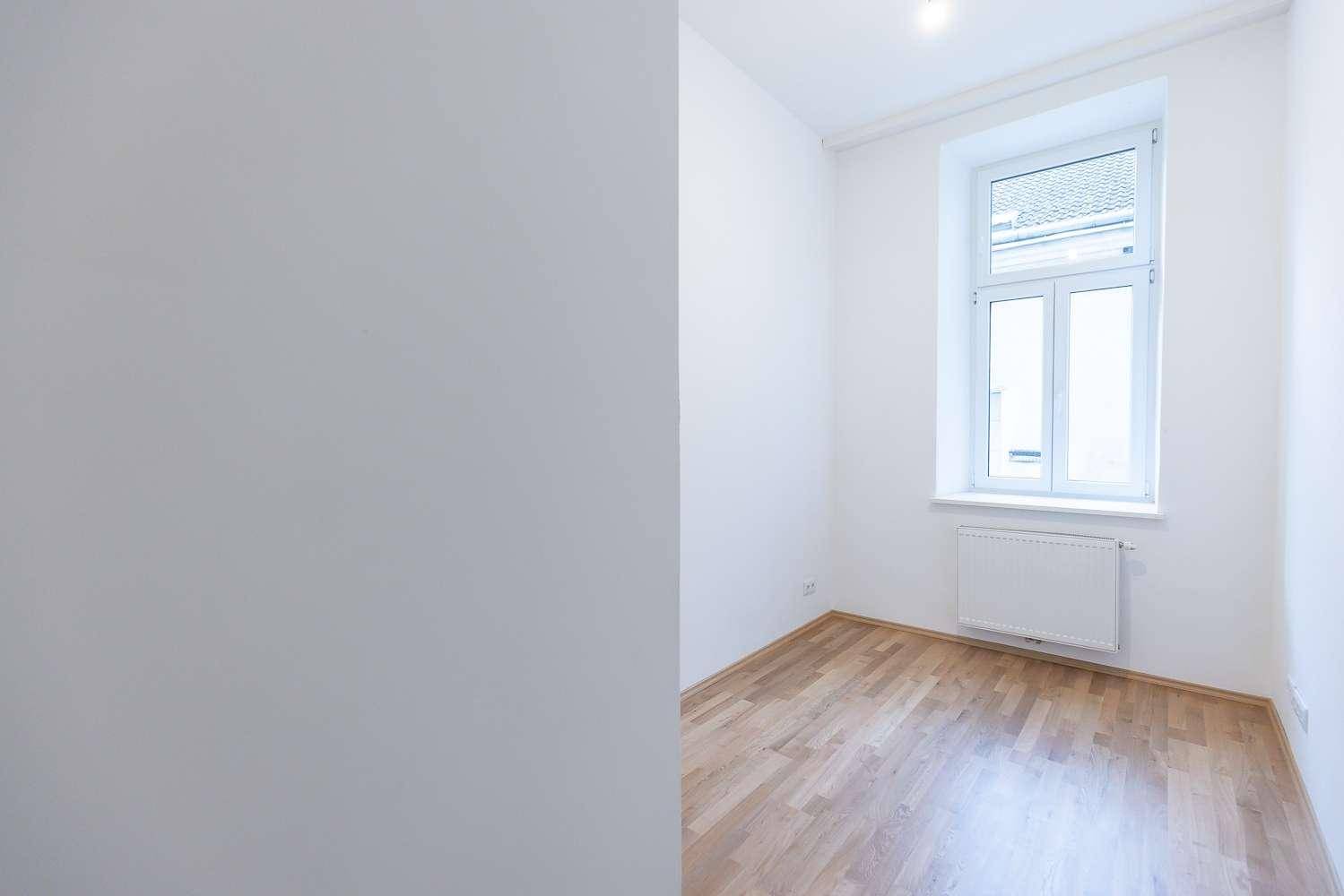 Helles Zimmer mit Parkettboden, weißen Wänden und einem Fenster, das viel Tageslicht bietet.
