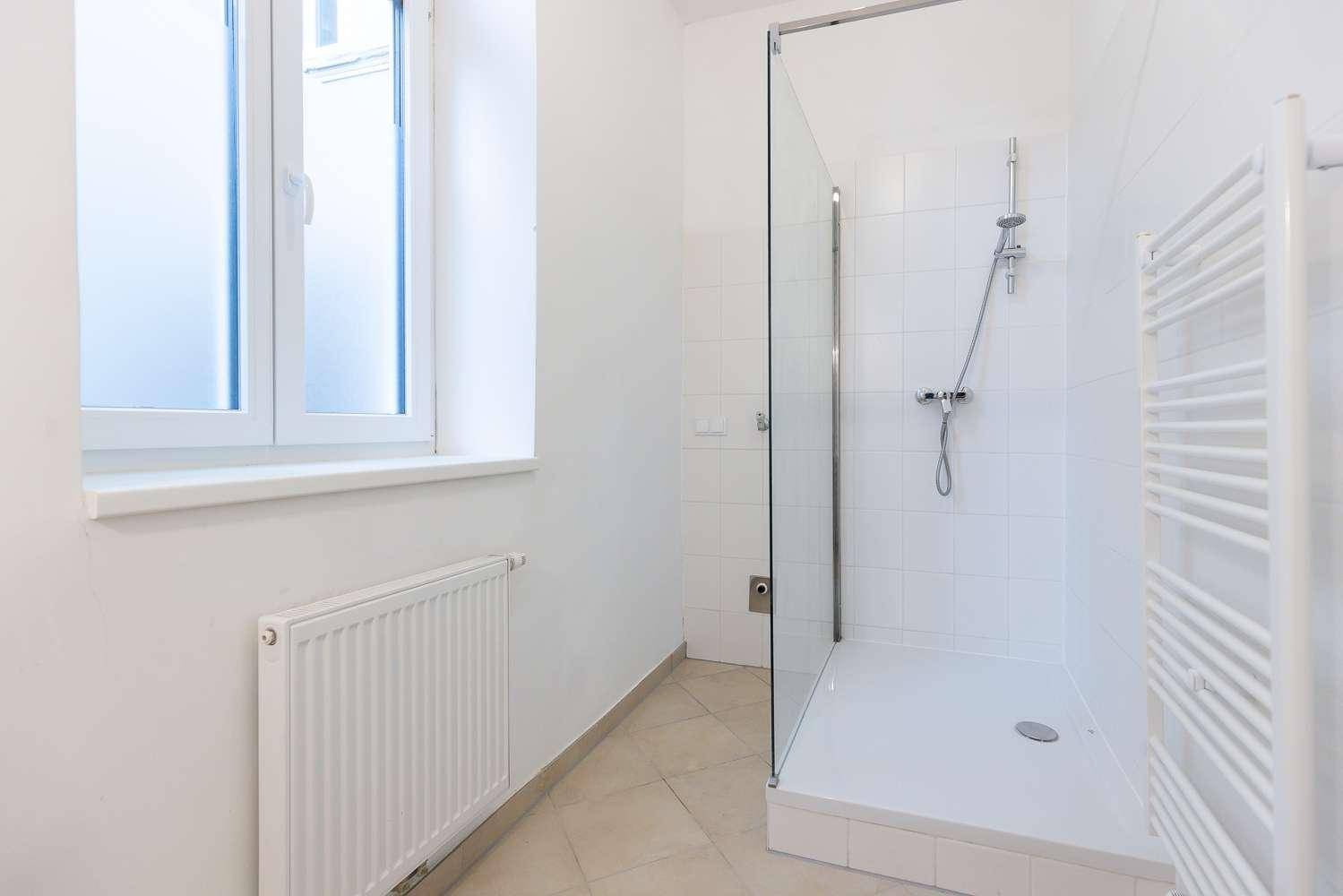Modernes Badezimmer mit Duschkabine, weißen Fliesen, Fenster und einem praktischen Handtuchheizkörper.