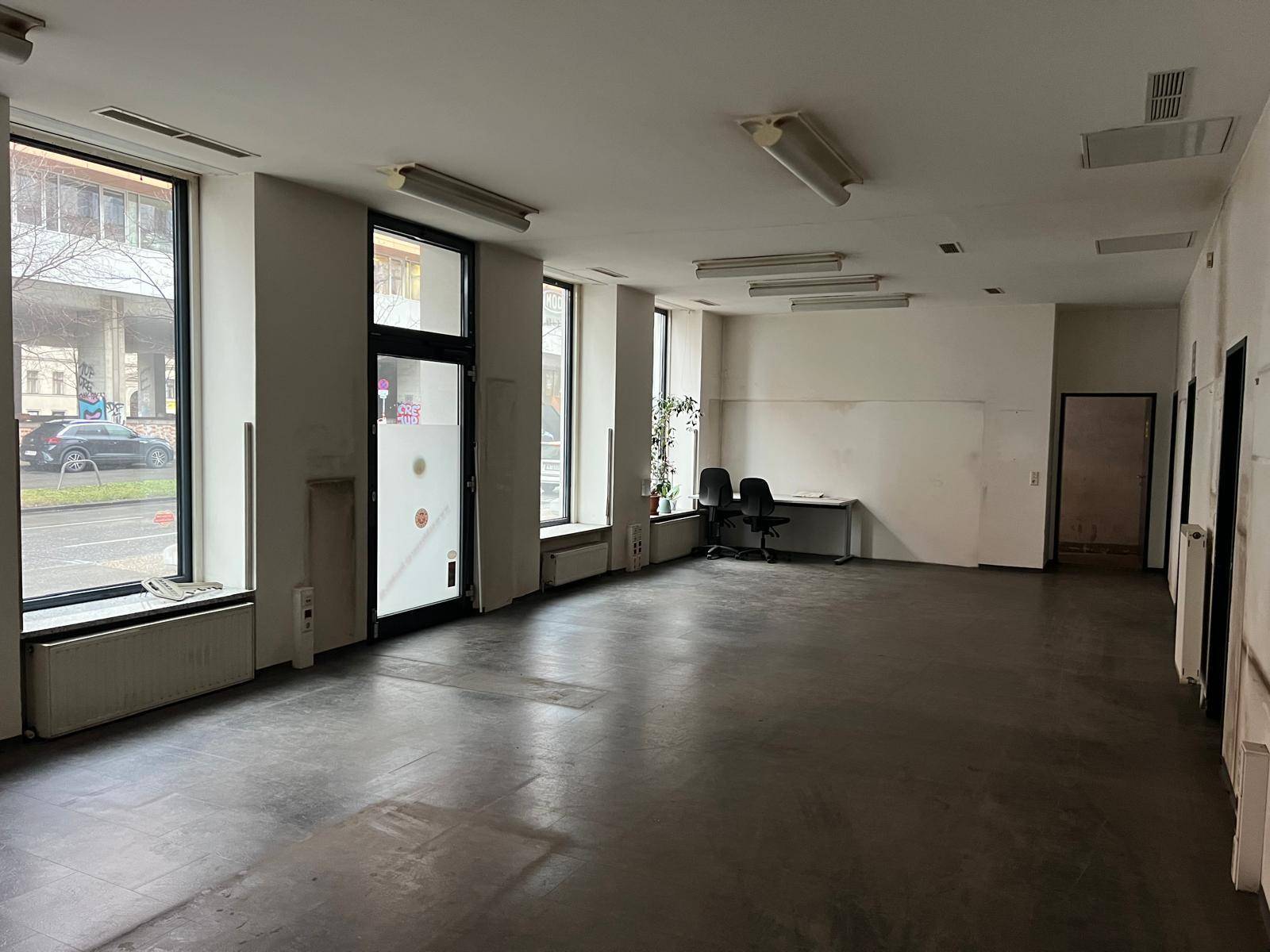 Geräumiger Geschäftsraum mit großen Fenstern zur Straße und dunklem Boden, der renovierungsbedürftig ist.