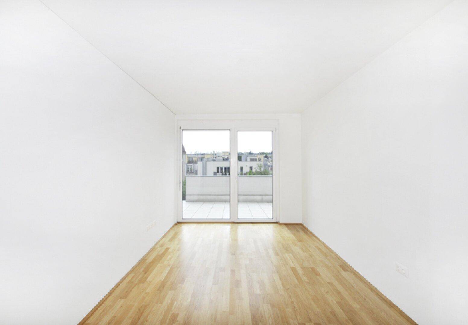 Heller, leerer Raum mit Holzboden und Zugang zu einem Balkon, ideal für Schlaf- oder Wohnzimmer.