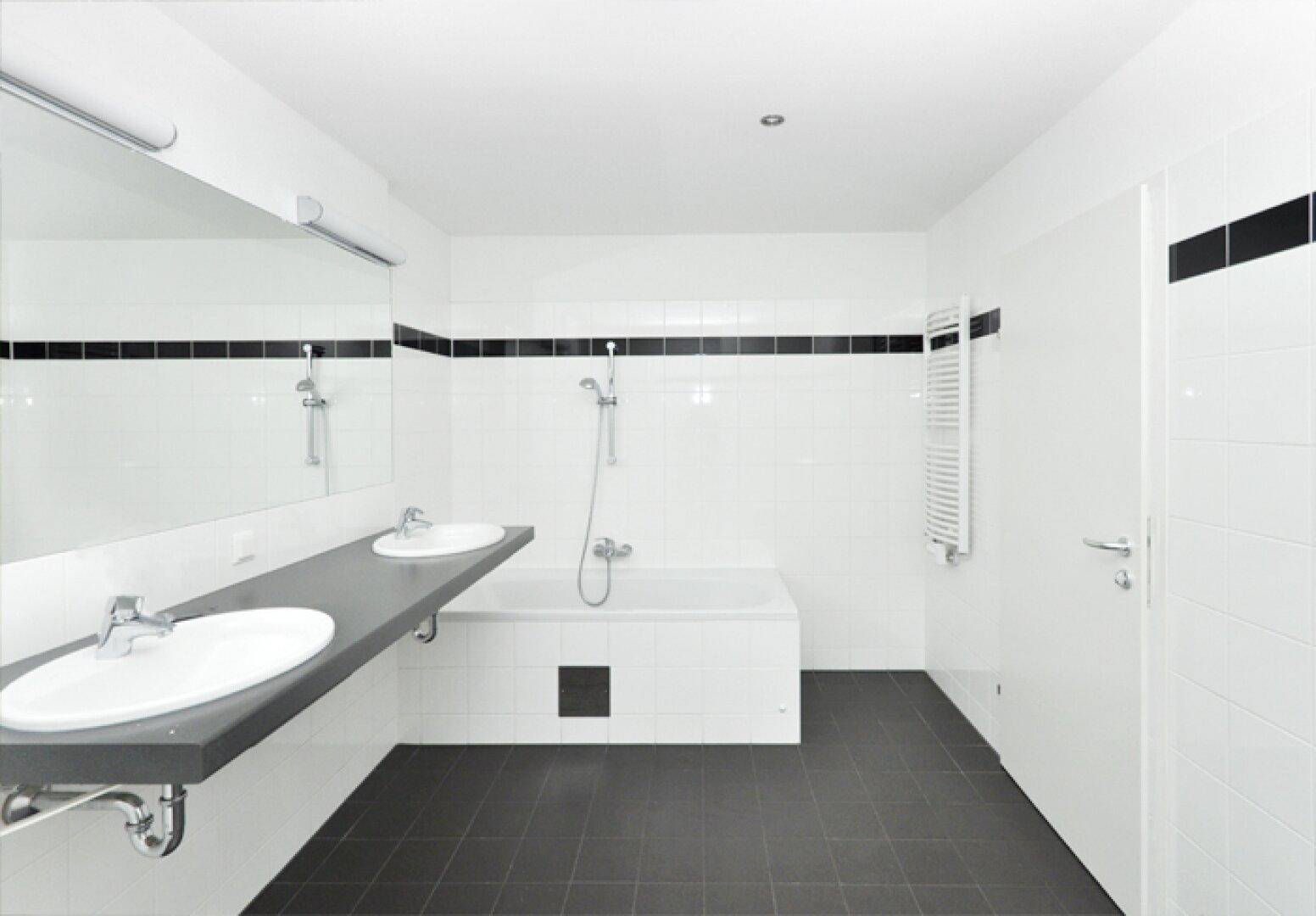 Modernes Badezimmer mit Doppelwaschbecken, Badewanne und schwarz-weißen Fliesen.