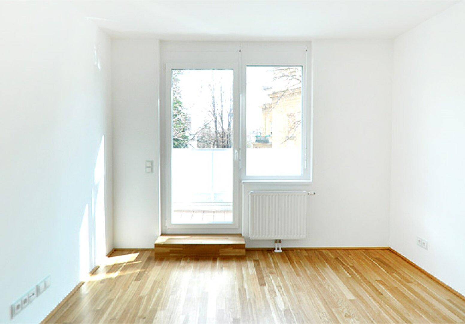 Heller Raum mit Parkettboden und direktem Zugang zu einem Balkon oder einer Terrasse.
