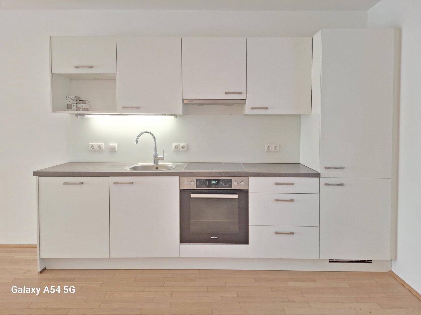 Moderne Einbauküche in Weiß mit integriertem Backofen und Kochfeld.