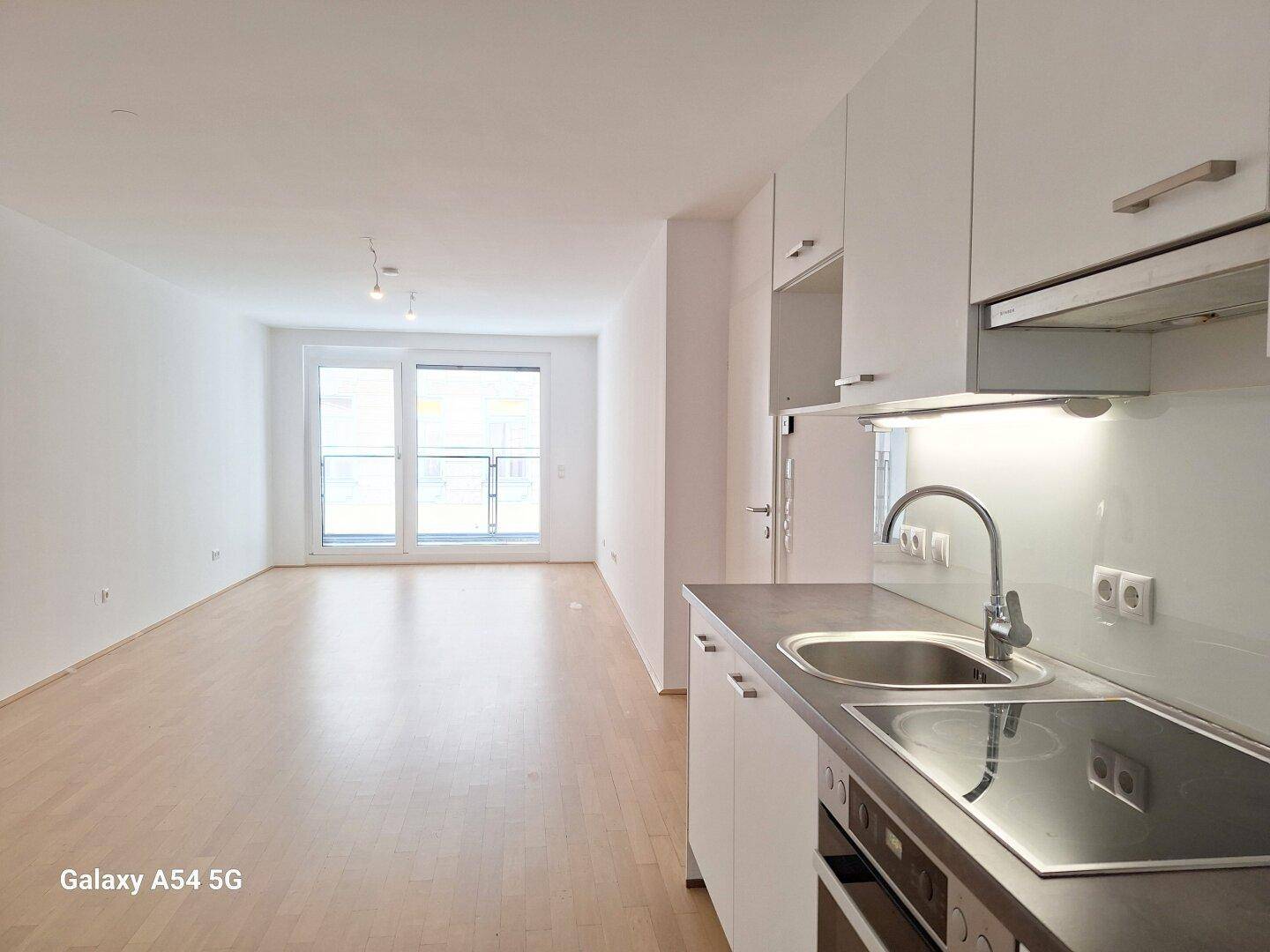 Helle, offene Wohnküche mit Einbauküche, Parkettboden und Zugang zum Balkon.