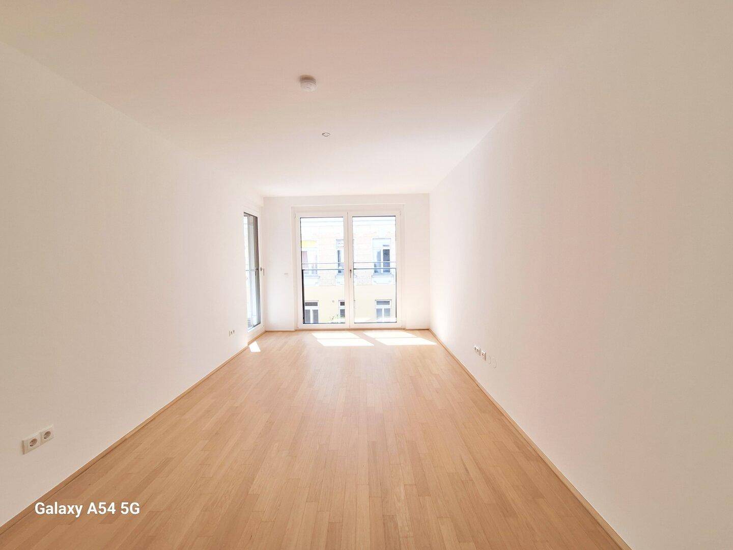 Lichtdurchfluteter, leerer Raum mit Parkettboden und Zugang zu einem französischen Balkon.