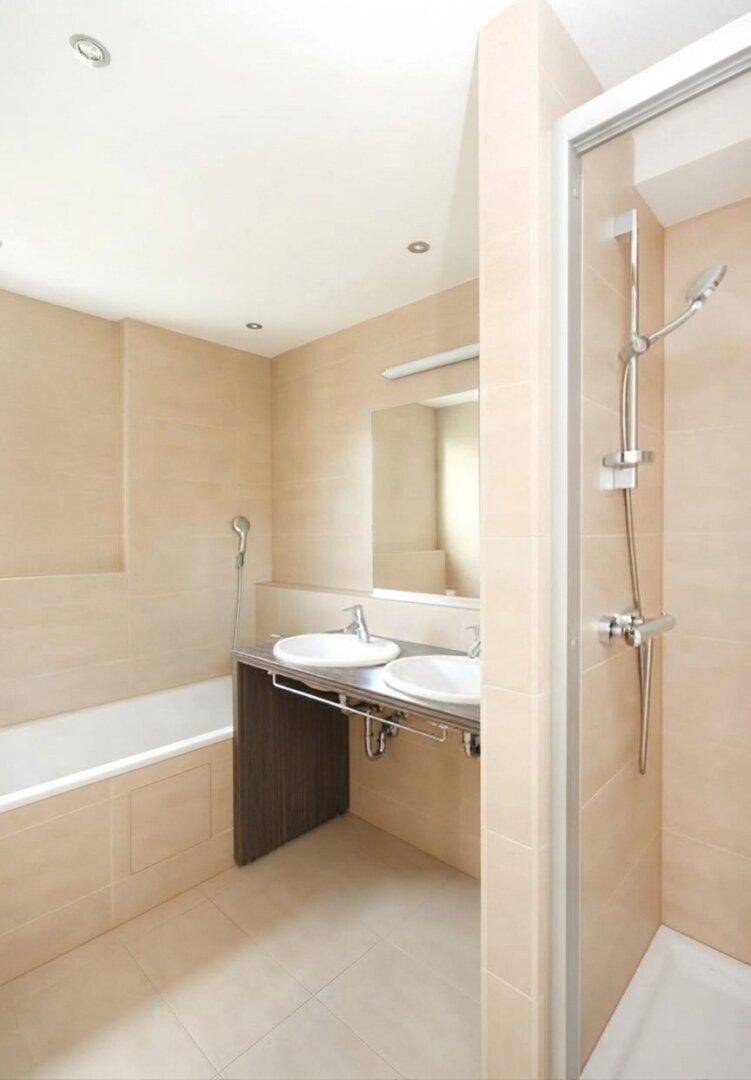 Modernes Badezimmer mit beigefarbenen Fliesen, Doppelwaschbecken und separater Dusche.
