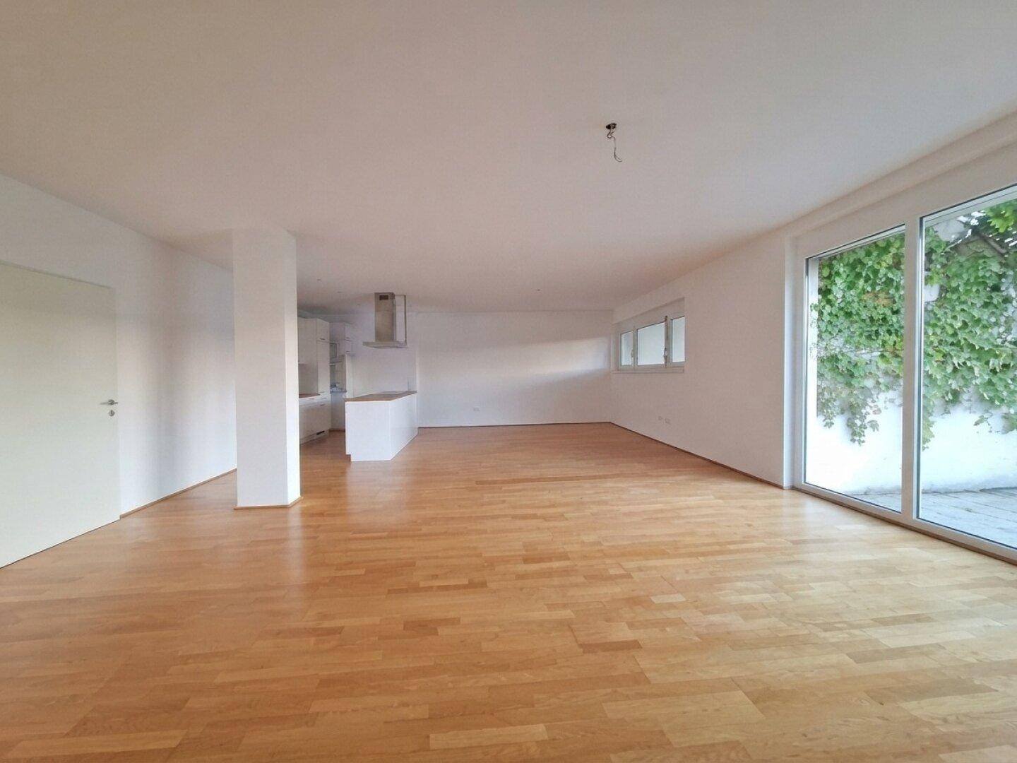 Geräumiger, leerer Wohn-Essbereich mit Holzboden und großen Fenstern, bereit zur individuellen Gestaltung.