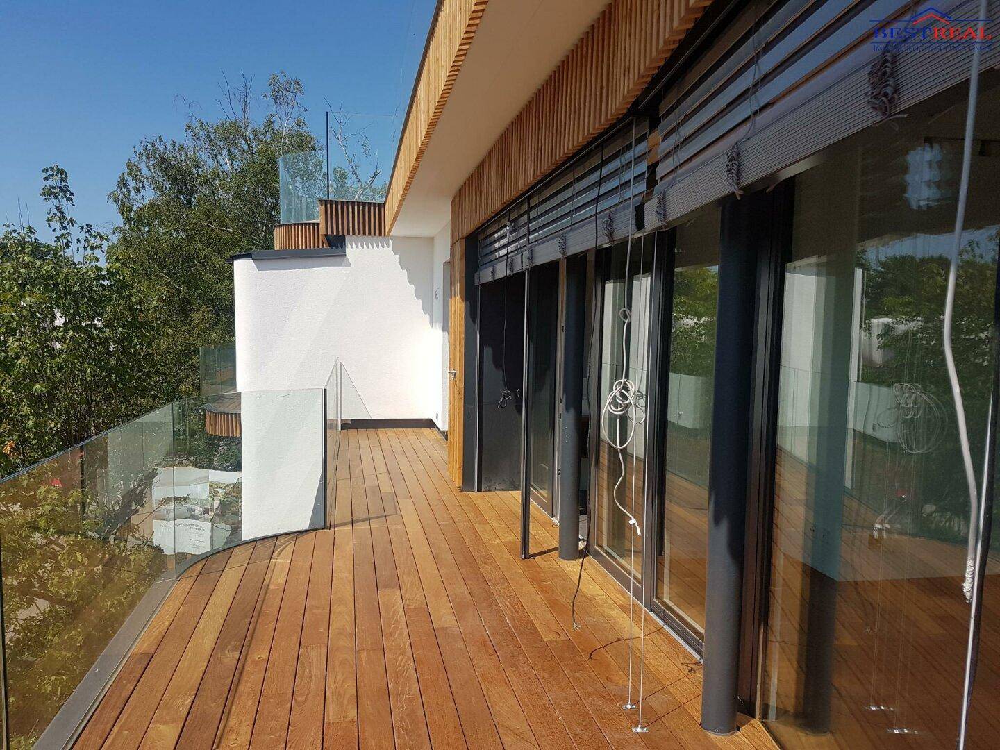 Moderne Holzterrasse mit Glasgeländer und Blick ins Grüne, ideal für Entspannung im Freien.