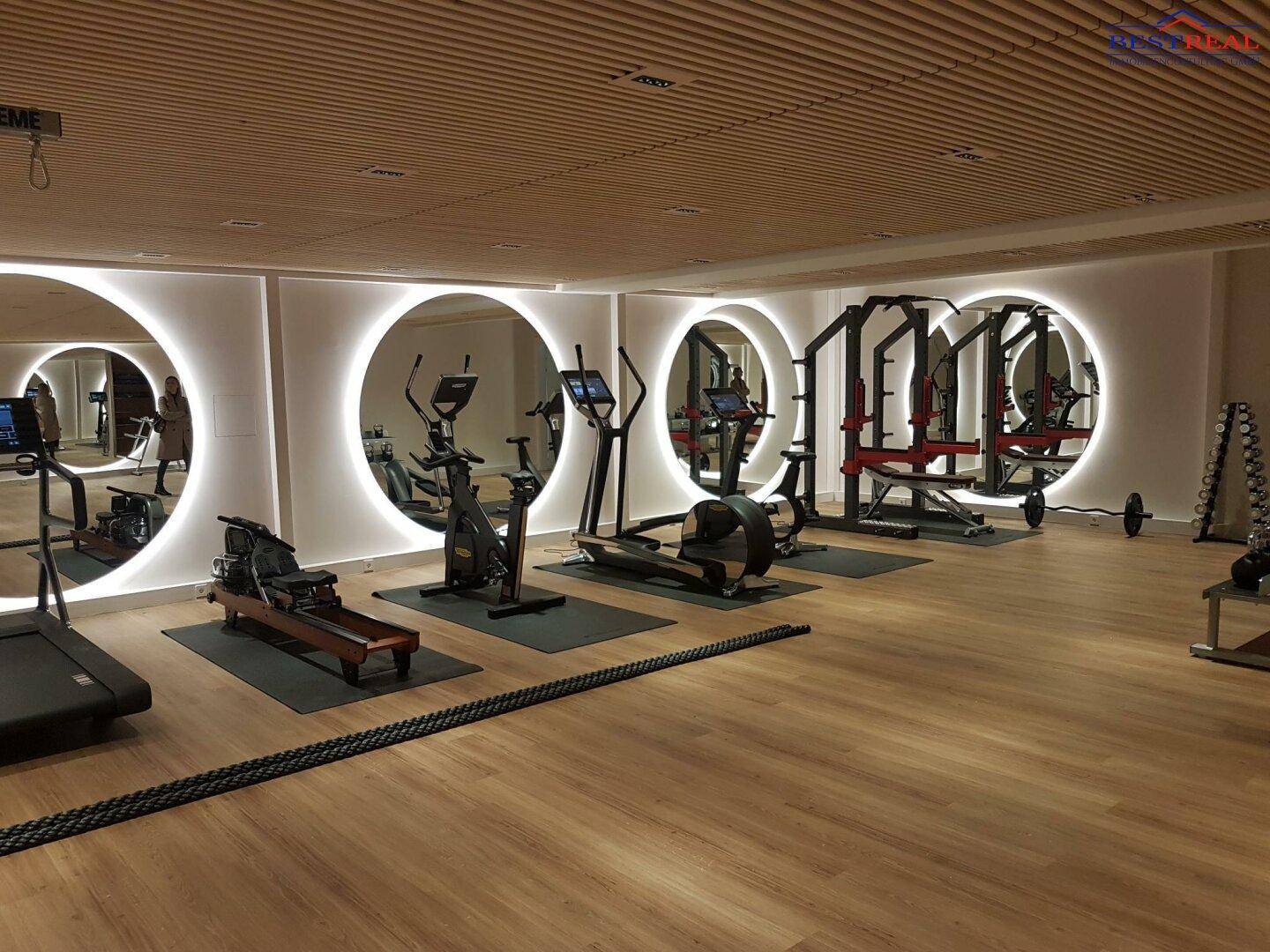 Moderner Fitnessraum mit einer Vielzahl an Trainingsgeräten, Holzdecke und stilvoller indirekter Beleuchtung.