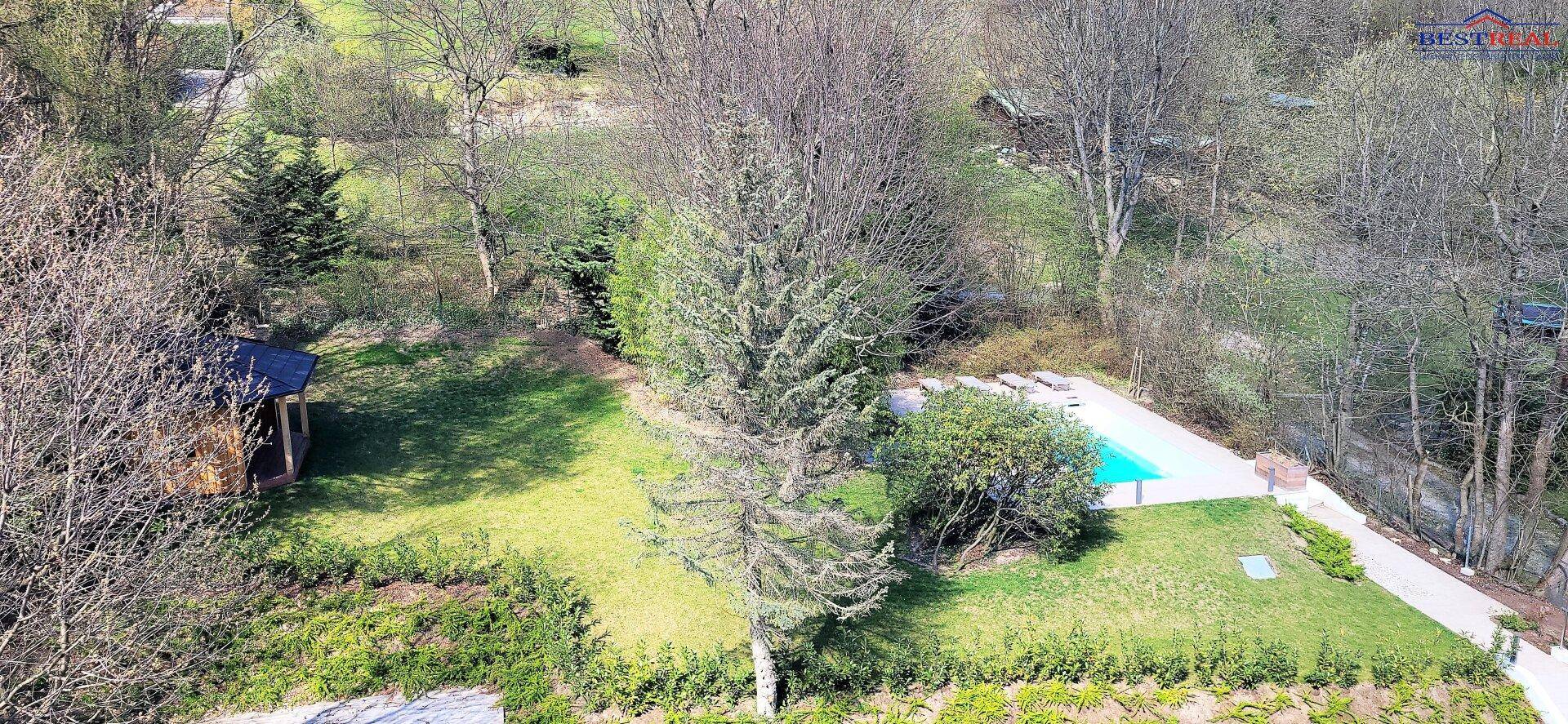 Luftaufnahme eines Anwesens mit großem Garten, Swimmingpool und Gartenhaus inmitten von Bäumen.