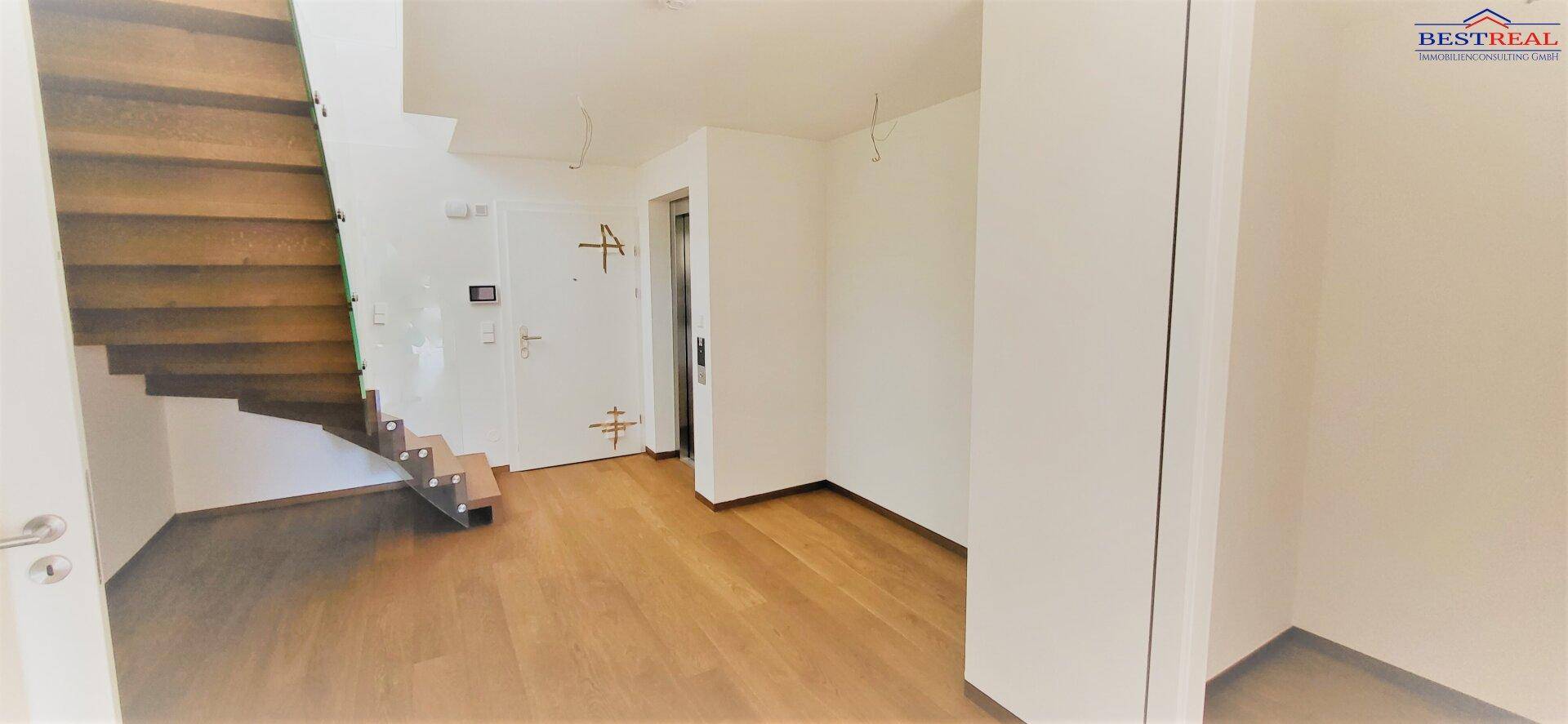 Eingangsbereich mit Holztreppe und Zugang zu einem Aufzug, hell und modern gestaltet.