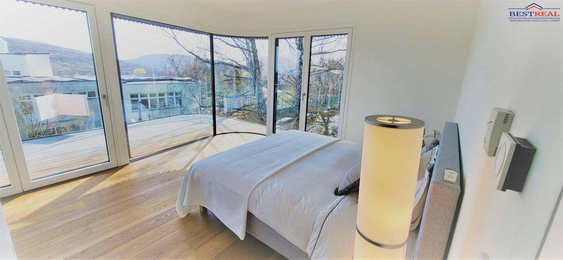 Schlafzimmer mit Bett und beeindruckenden, raumhohen Fenstern, die viel Licht spenden und Weitblick bieten.