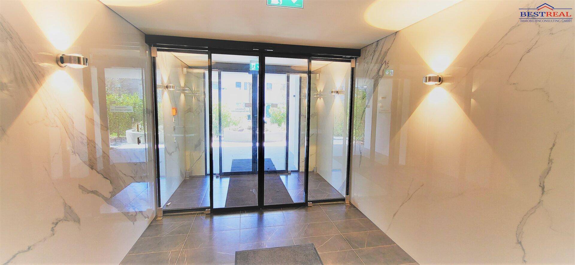 Moderner Eingangsbereich mit automatischen Glastüren und eleganten Marmorfliesen an den Wänden.