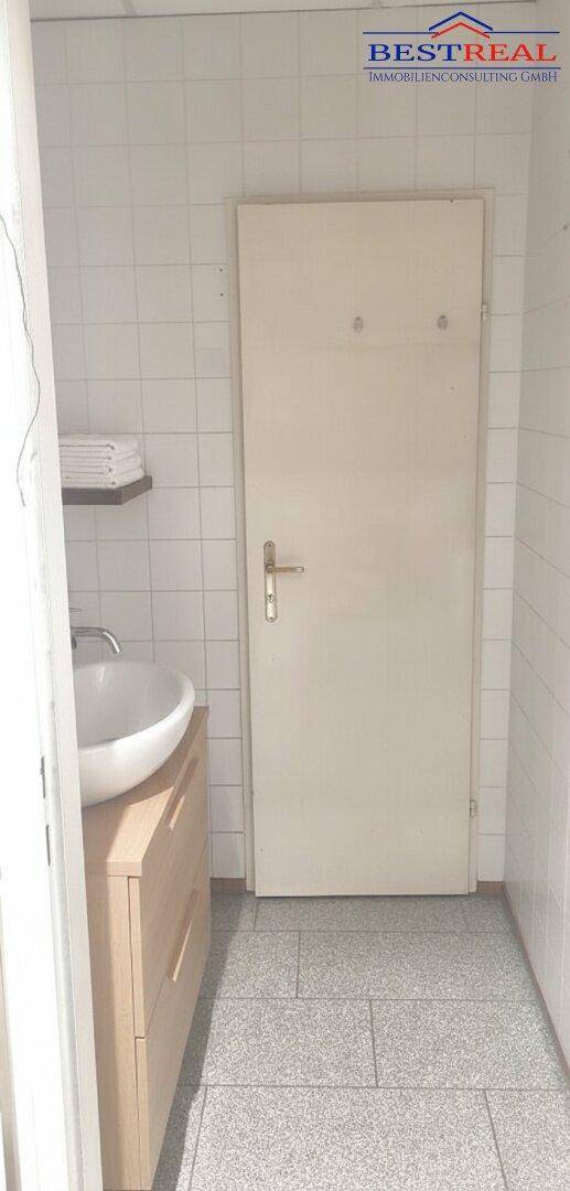 Kleines Badezimmer mit modernem Waschbecken auf Holzunterschrank und weißen Wandfliesen.
