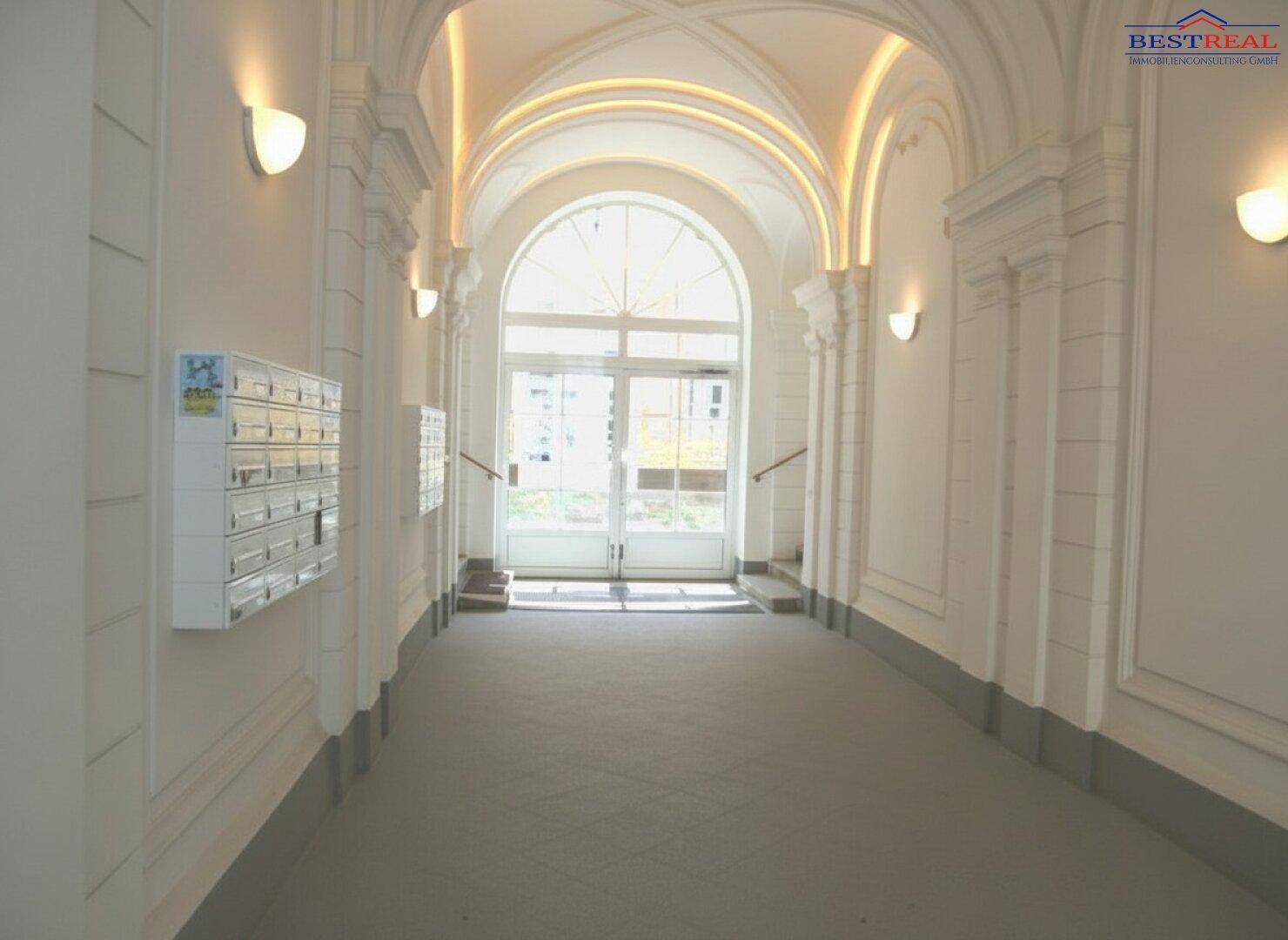 Ein langer, heller Eingangsbereich mit Gewölbedecke, Fliesenboden und Briefkästen an der Wand.