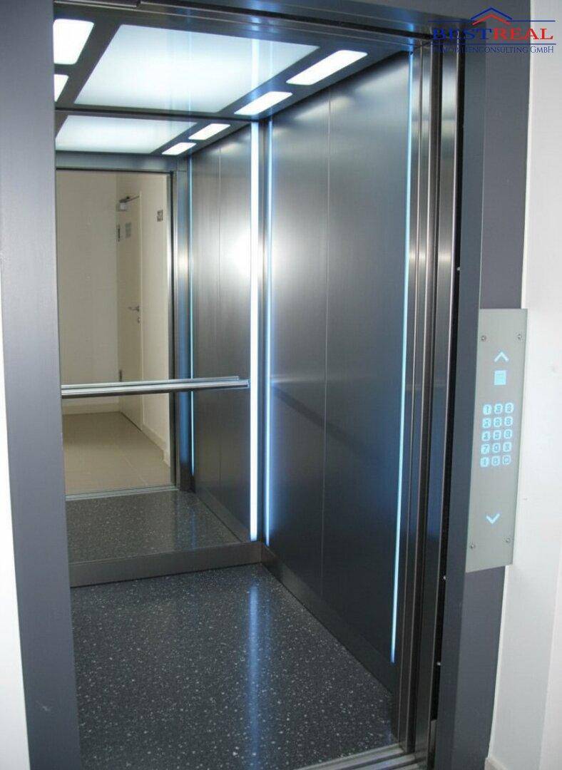 Ein moderner Aufzug mit Edelstahlwänden, beleuchteten Paneelen und einem dunklen Boden.