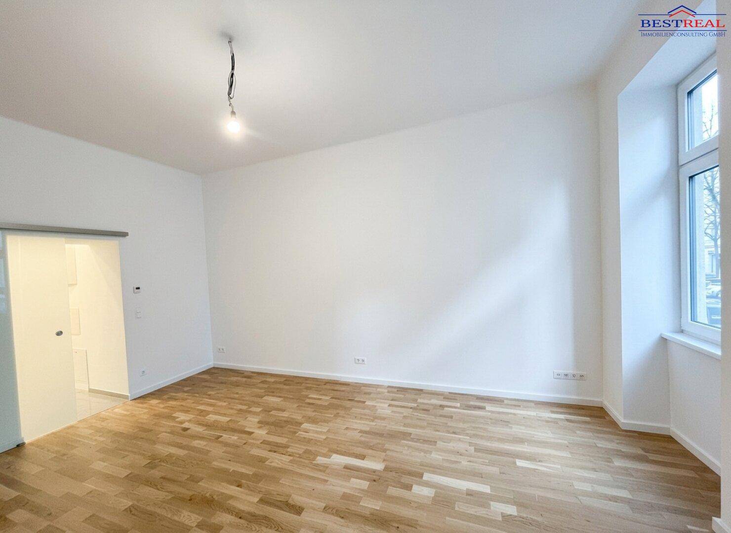 Helles, leeres Zimmer mit Parkettboden und großem Fenster, bereit zur individuellen Gestaltung.