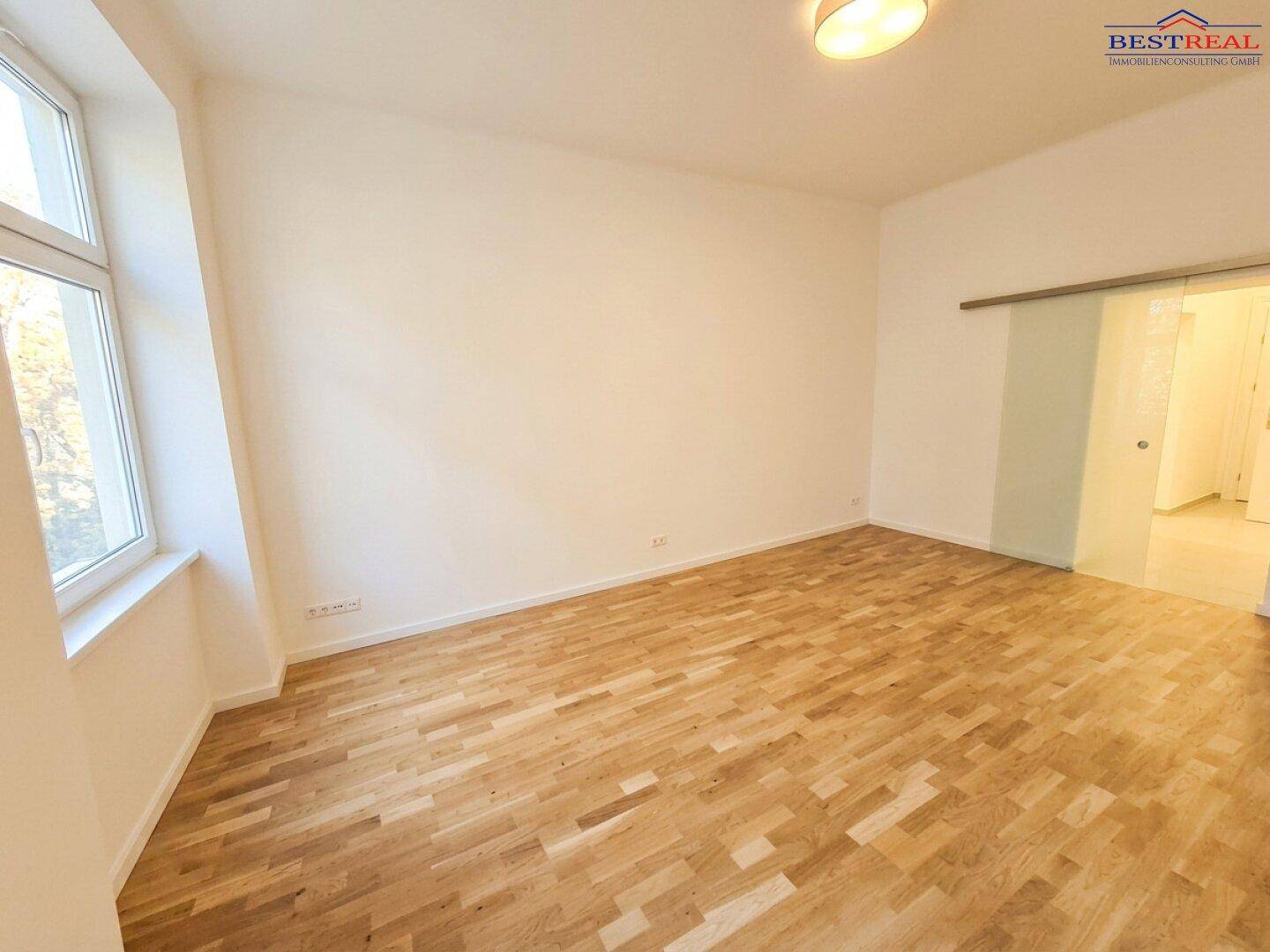 Lichtdurchfluteter Raum mit Parkettboden und Schiebetür, bietet flexible Nutzungsmöglichkeiten.