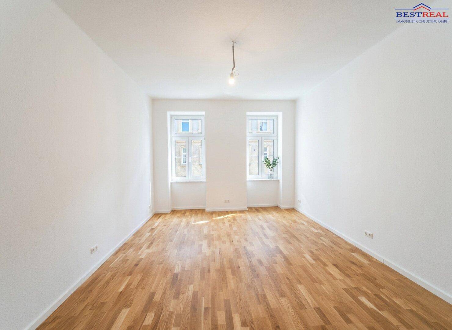 Helles, leeres Zimmer mit Parkettboden und zwei Fenstern, bereit zur individuellen Gestaltung.