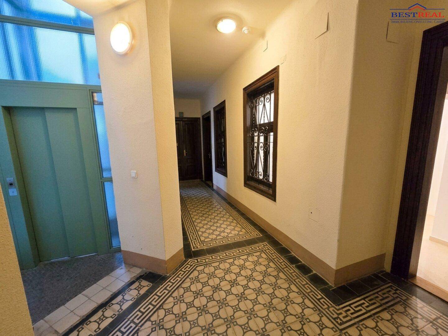 Historischer Flur mit aufwendigem Fliesenboden und einem Aufzug, der den Zugang erleichtert.